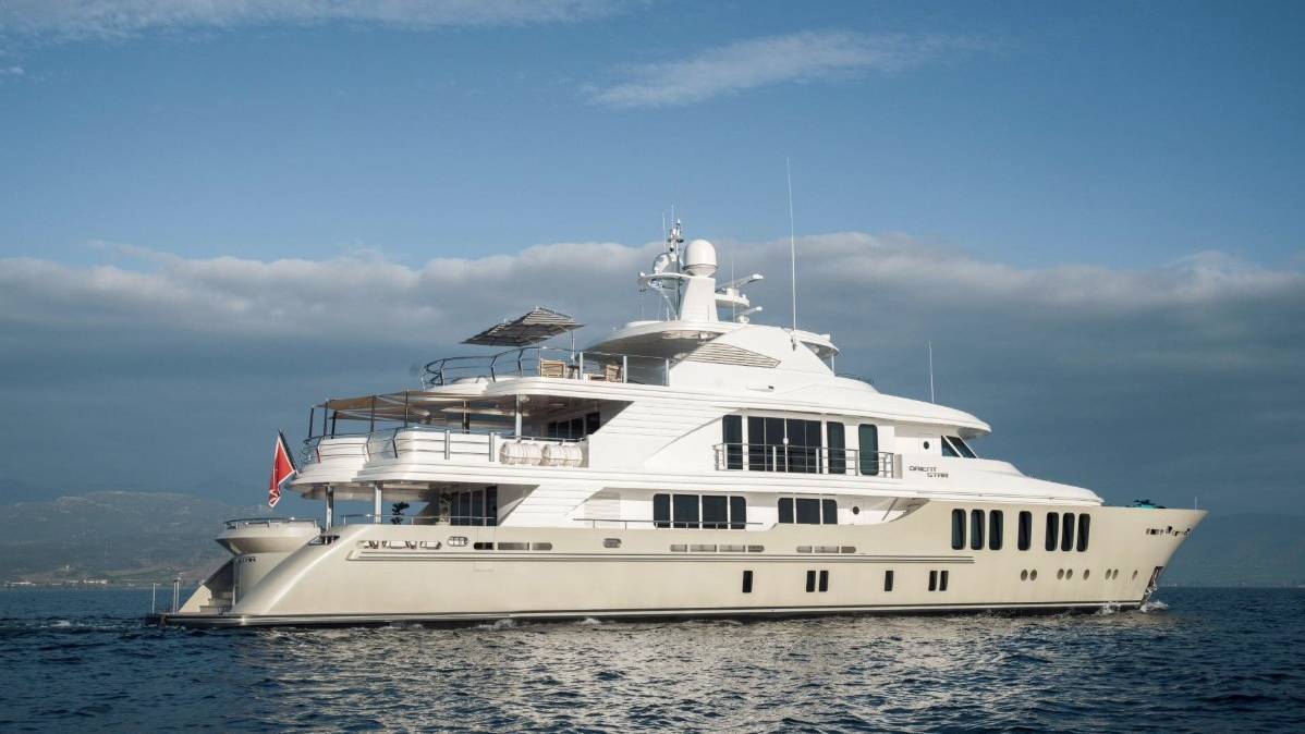 A luxurious yacht glides through calm blue waters under a partly cloudy sky.