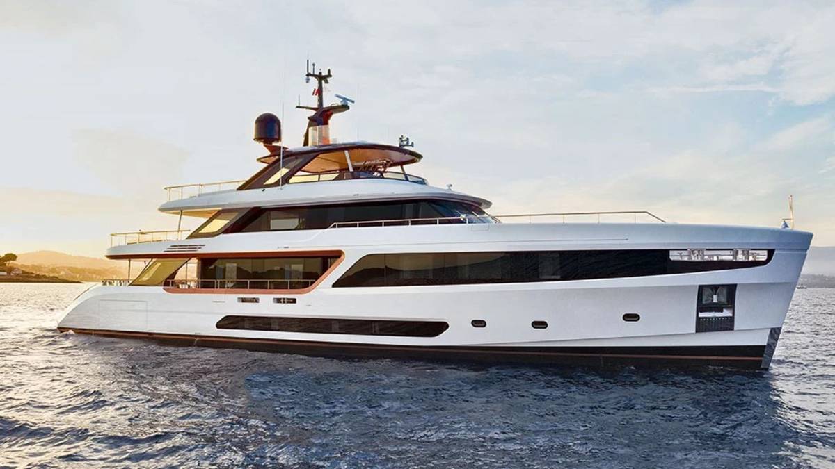 A sleek, modern white yacht glides across calm blue waters near a sun-drenched coastline.