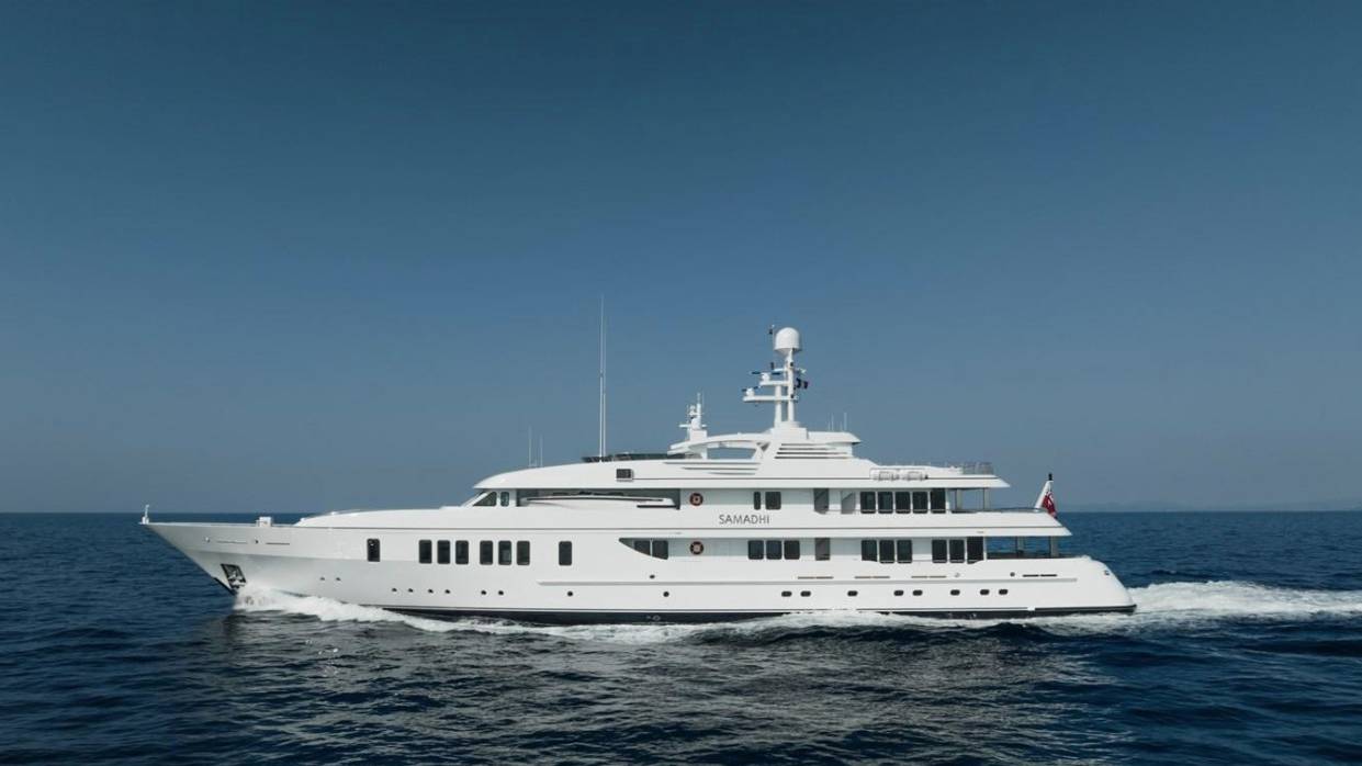 A large white yacht cruises through calm blue water with a clear blue sky in the background.