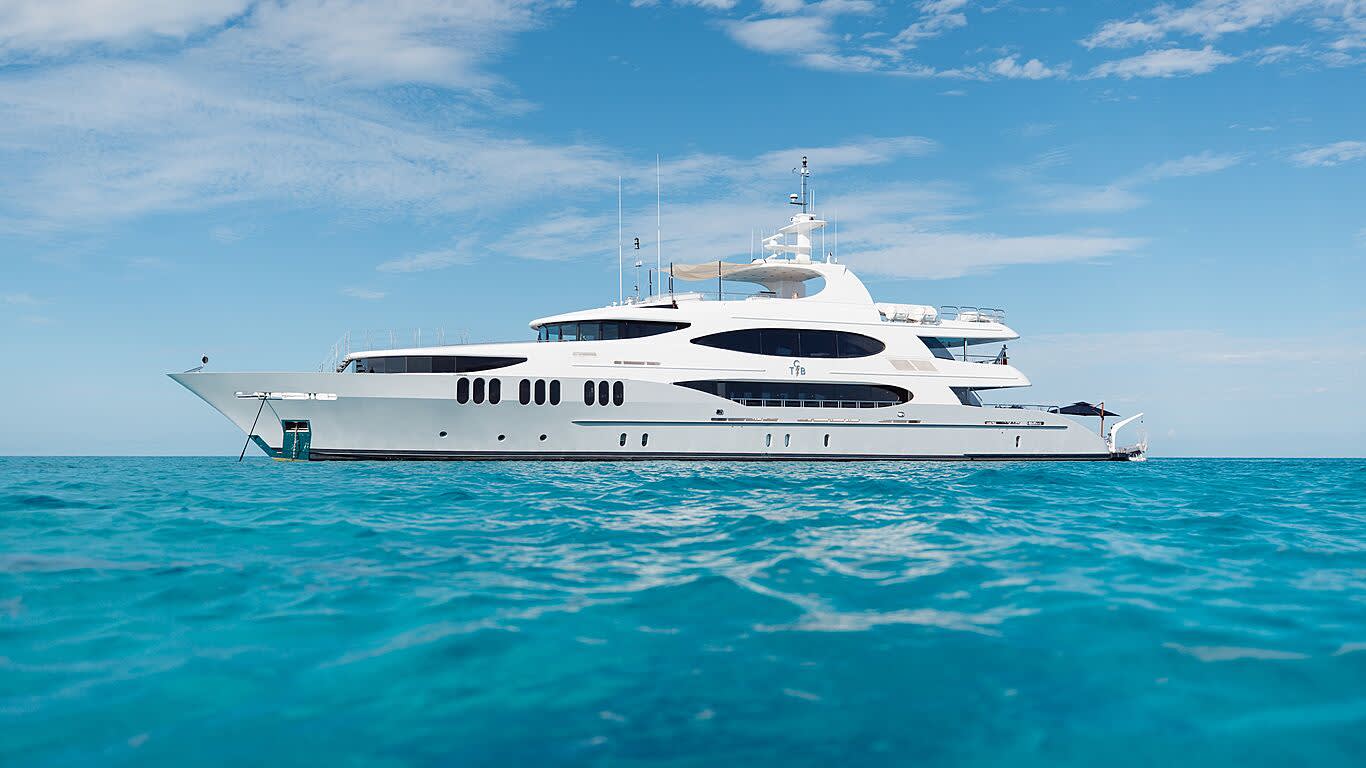 A large white yacht floats on turquoise water under a bright blue sky with scattered clouds.