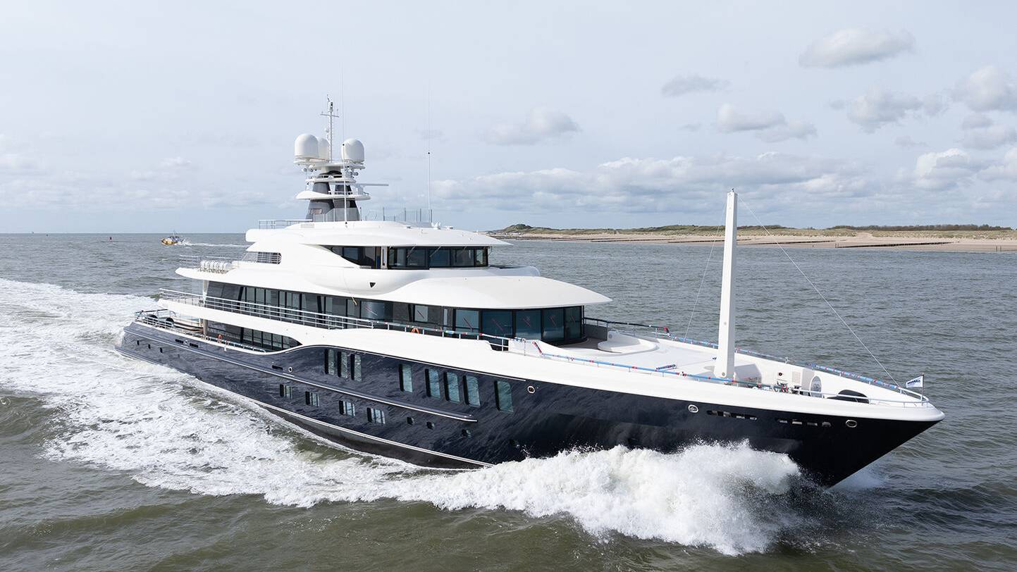 A sleek, dark-hulled superyacht cuts through choppy waters under a cloudy sky.