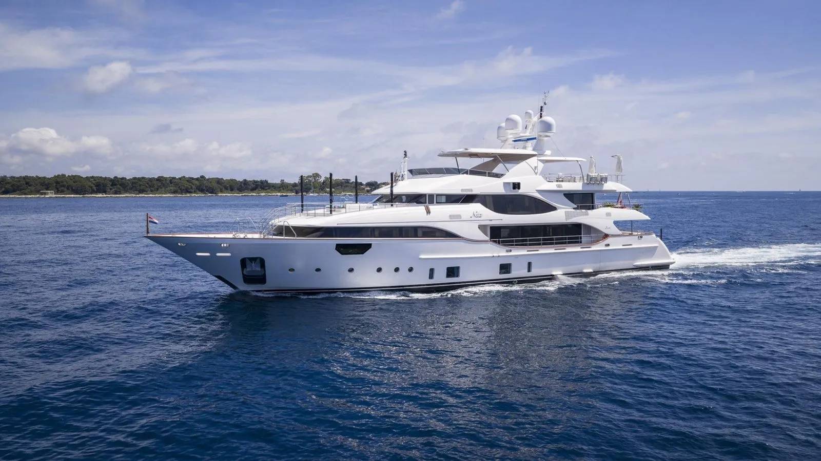 A sleek white yacht glides through the azure waters under a bright blue sky.