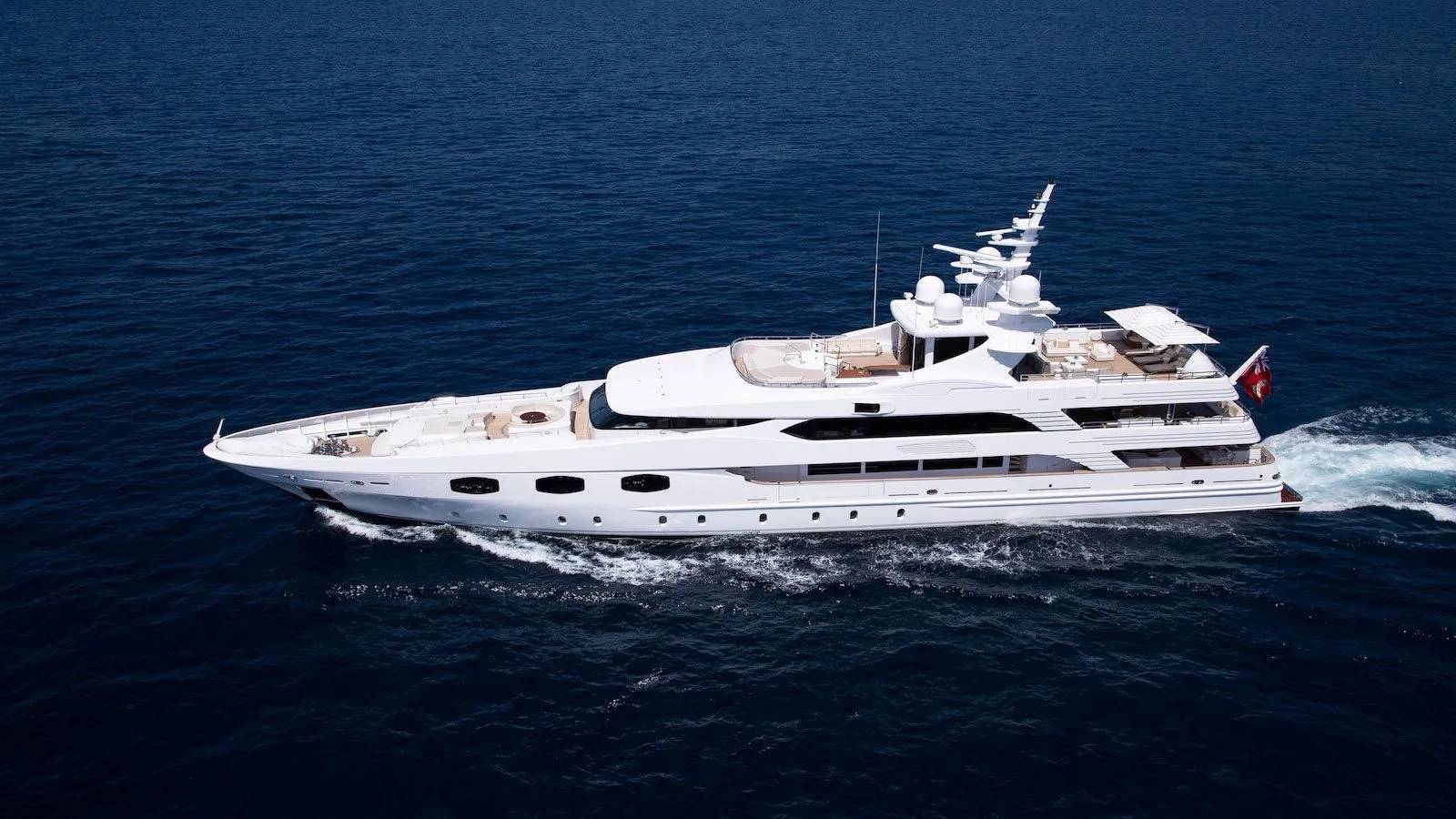 A luxurious white yacht glides through the deep blue ocean, leaving a foamy wake behind it.