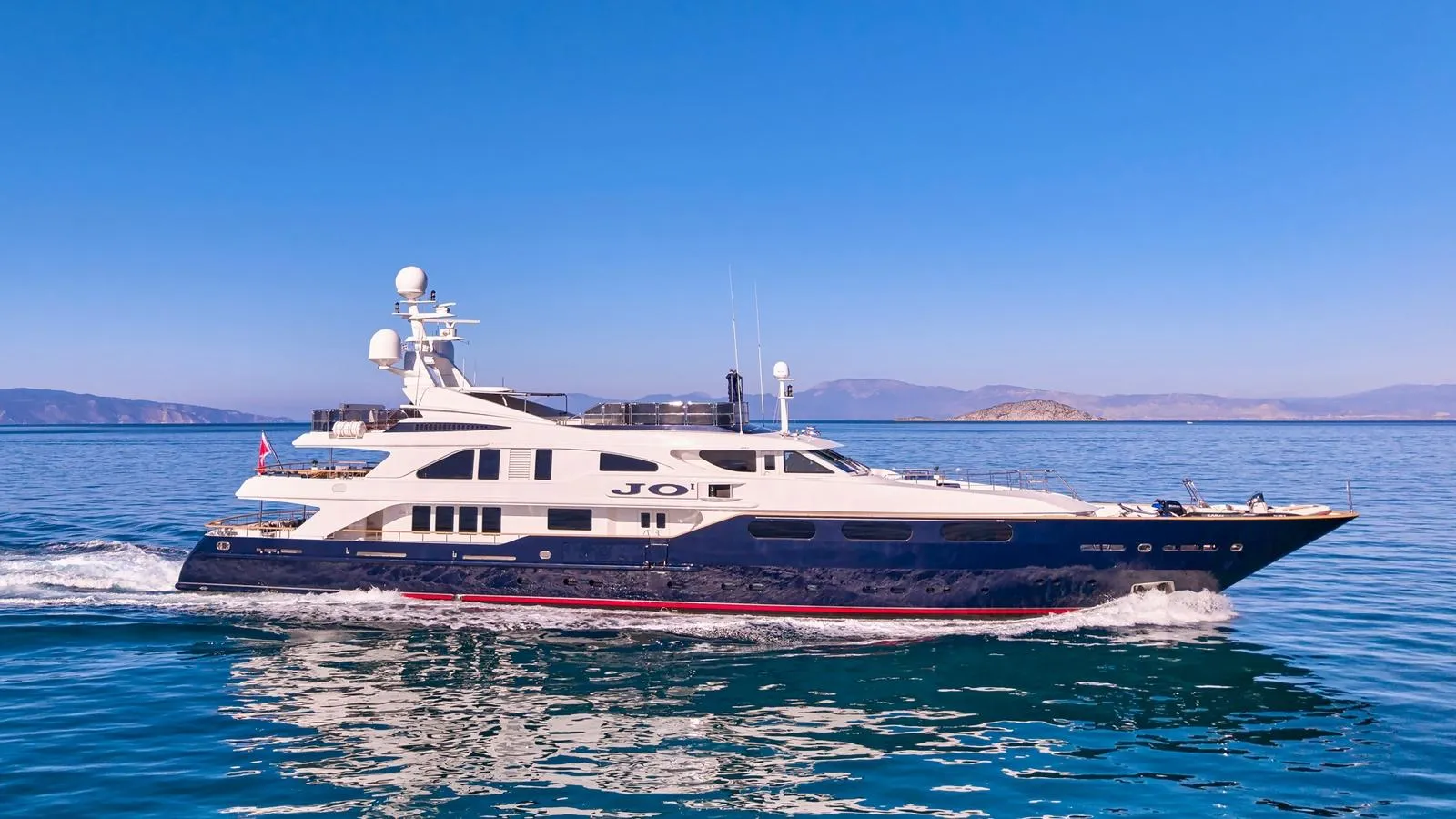 A sleek navy and white yacht cruises through the sparkling blue waters under a clear sky.