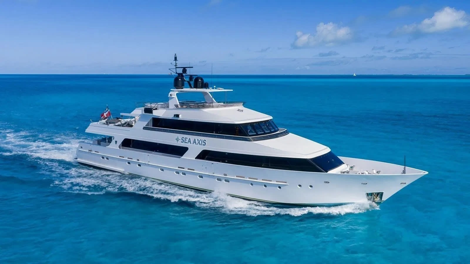 A large white yacht cruises through turquoise waters under a bright blue sky with scattered clouds.