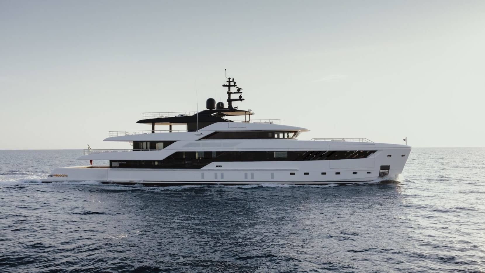 A sleek white superyacht glides through the deep blue ocean under a clear sky.