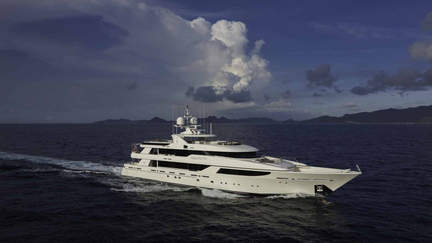 A sleek white yacht cruises through the deep blue ocean under a dramatic cloudy sky.