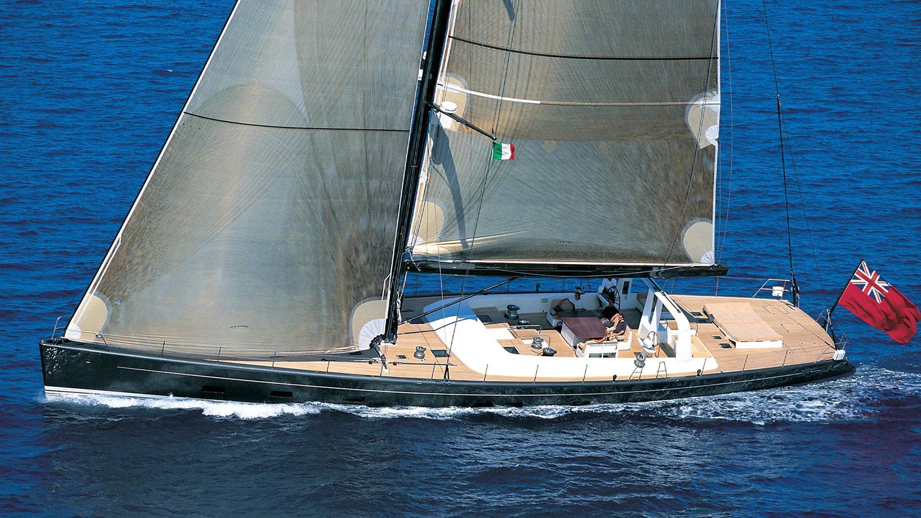 A sleek, dark sailboat with full sails glides across a deep blue ocean, its wake trailing behind it.