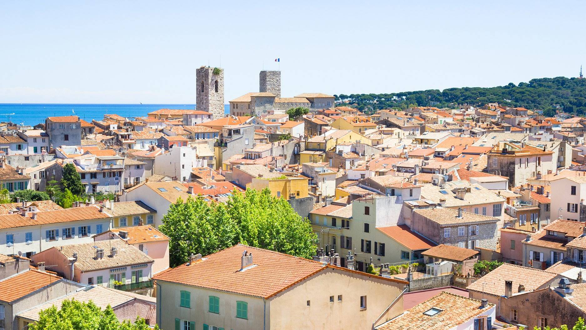 A panoramic view captures the charming terracotta rooftops and ancient stone towers of a sun-drenched coastal town.