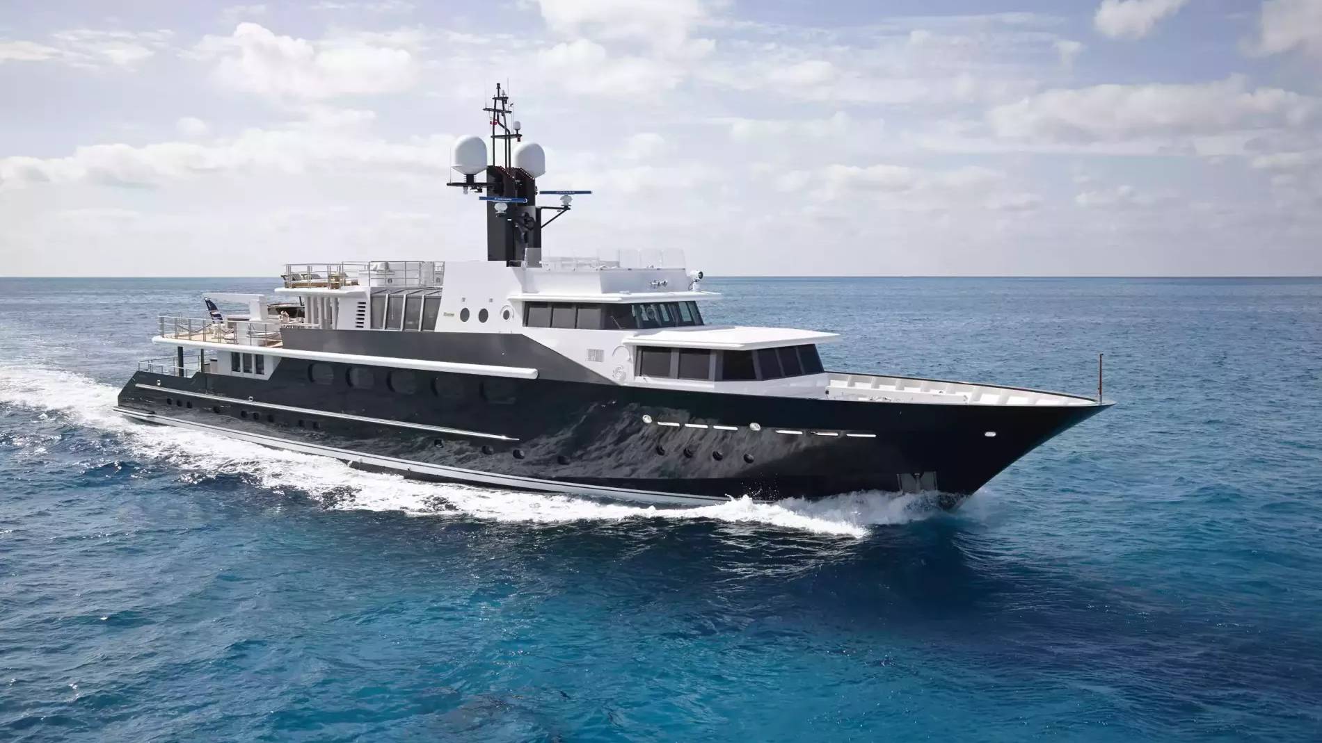 A sleek black and white yacht glides through the vibrant blue ocean under a cloudy sky.