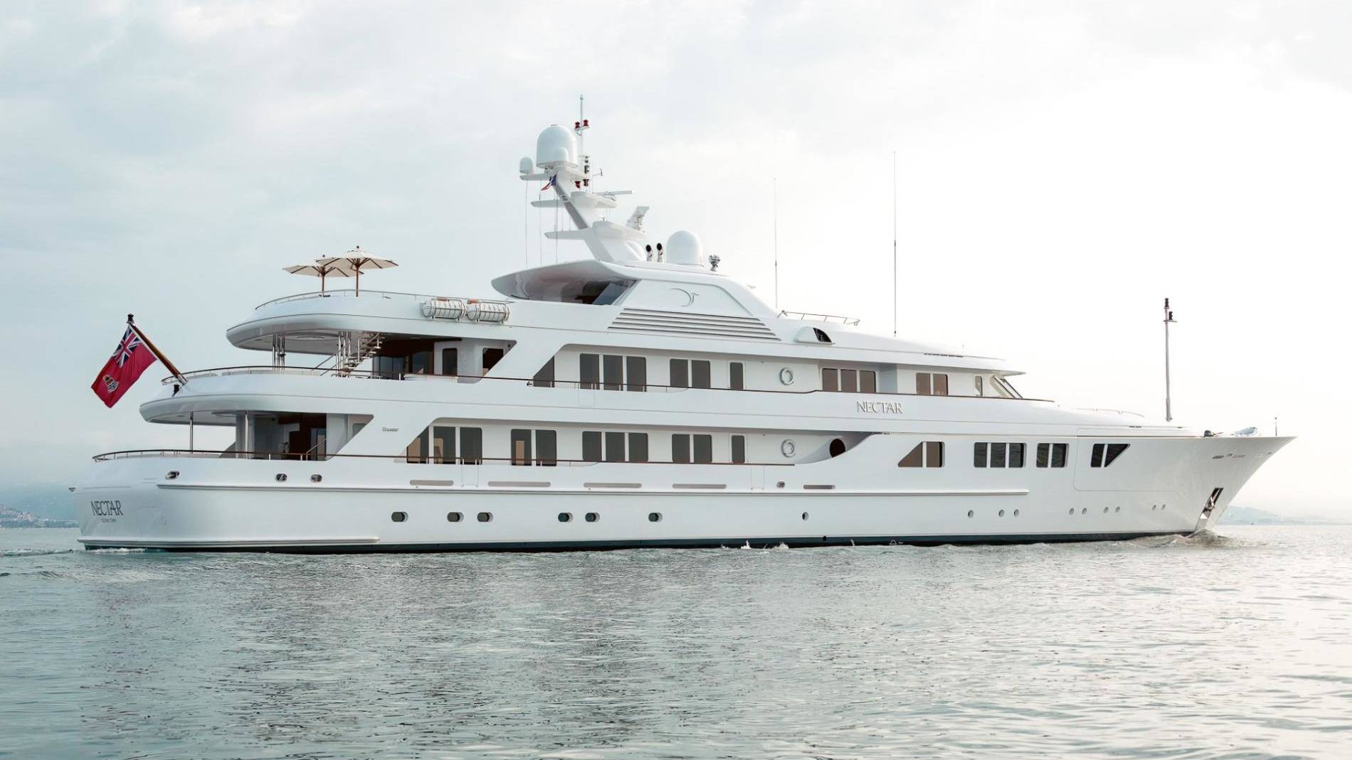 The luxurious white yacht Nectar glides gracefully across the calm, shimmering water under a bright sky.