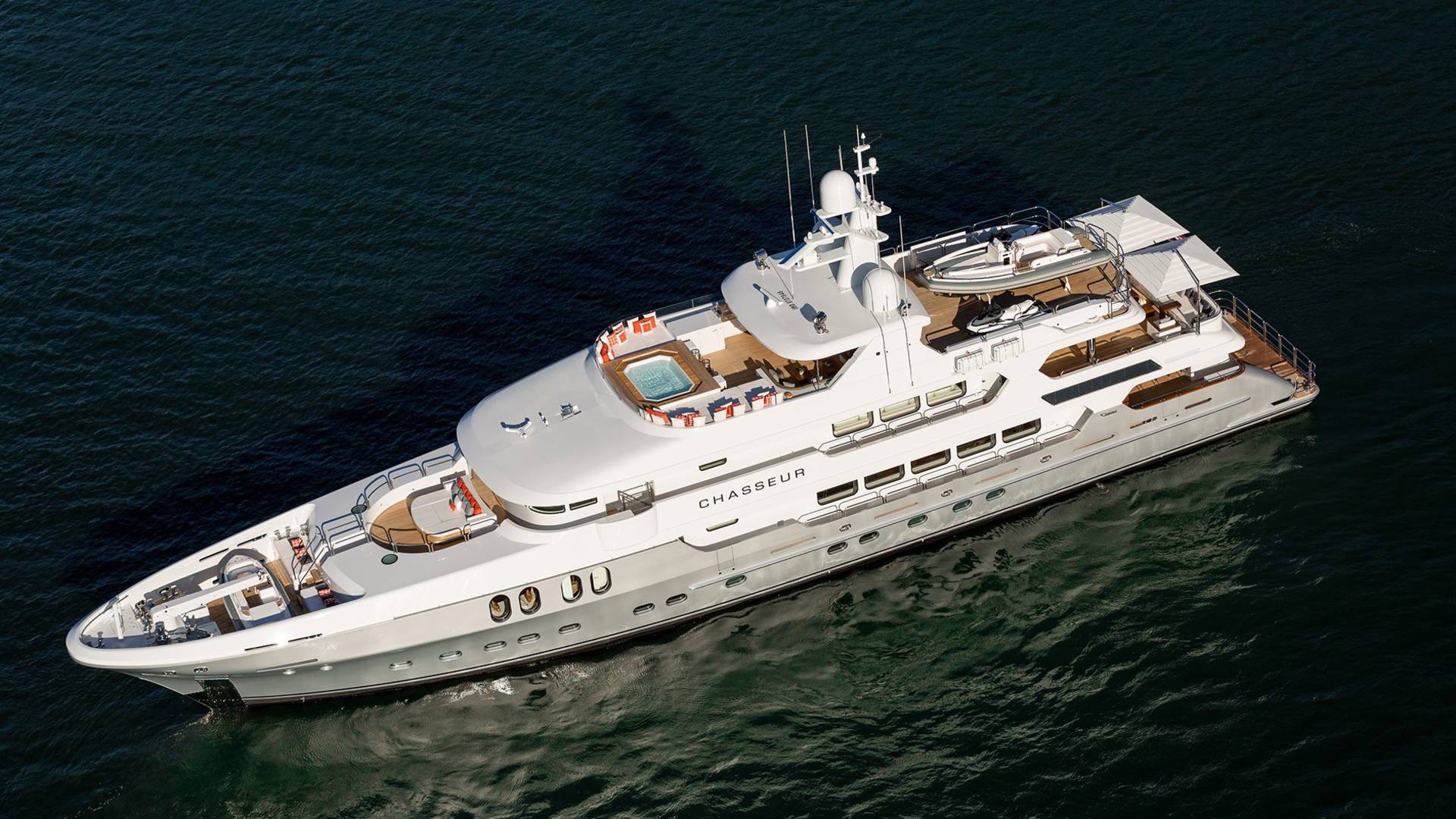 The luxurious yacht Chasseur glides through dark waters, featuring a sundeck with a hot tub and ample seating.