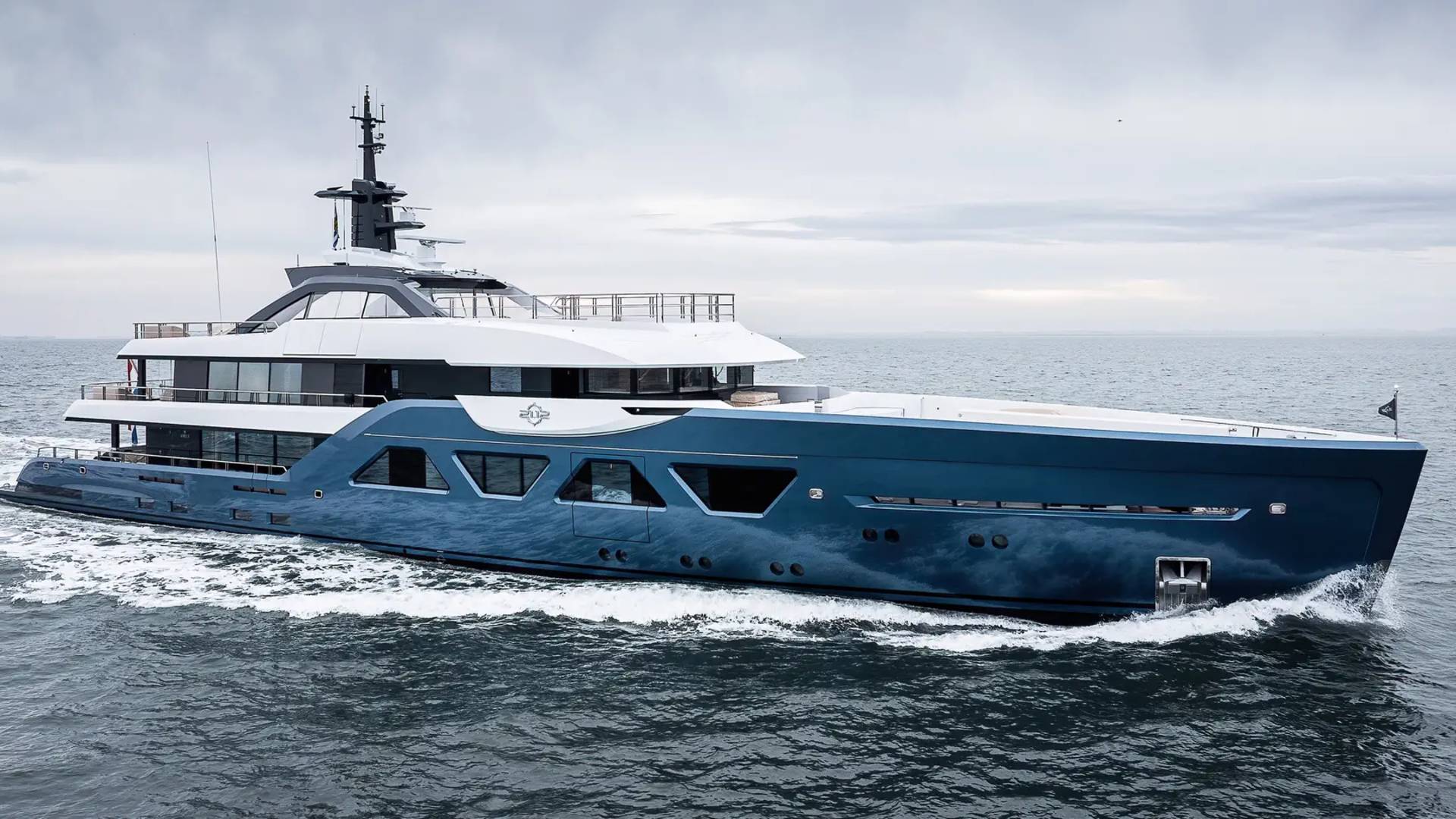 A large, modern yacht with a sleek, angular design is sailing across the open ocean under a cloudy sky.