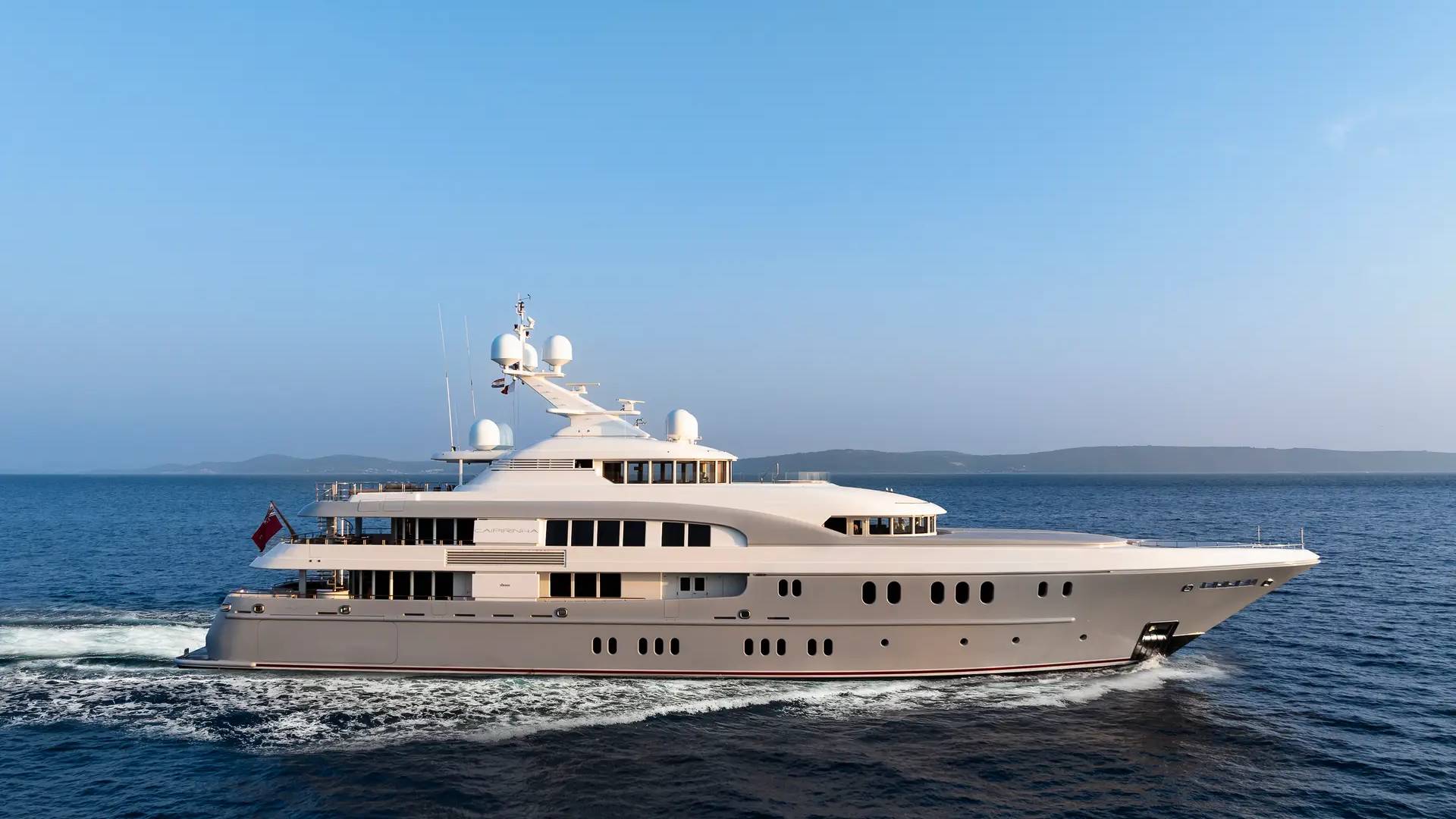 A sleek, modern yacht glides through calm blue waters under a clear sky.