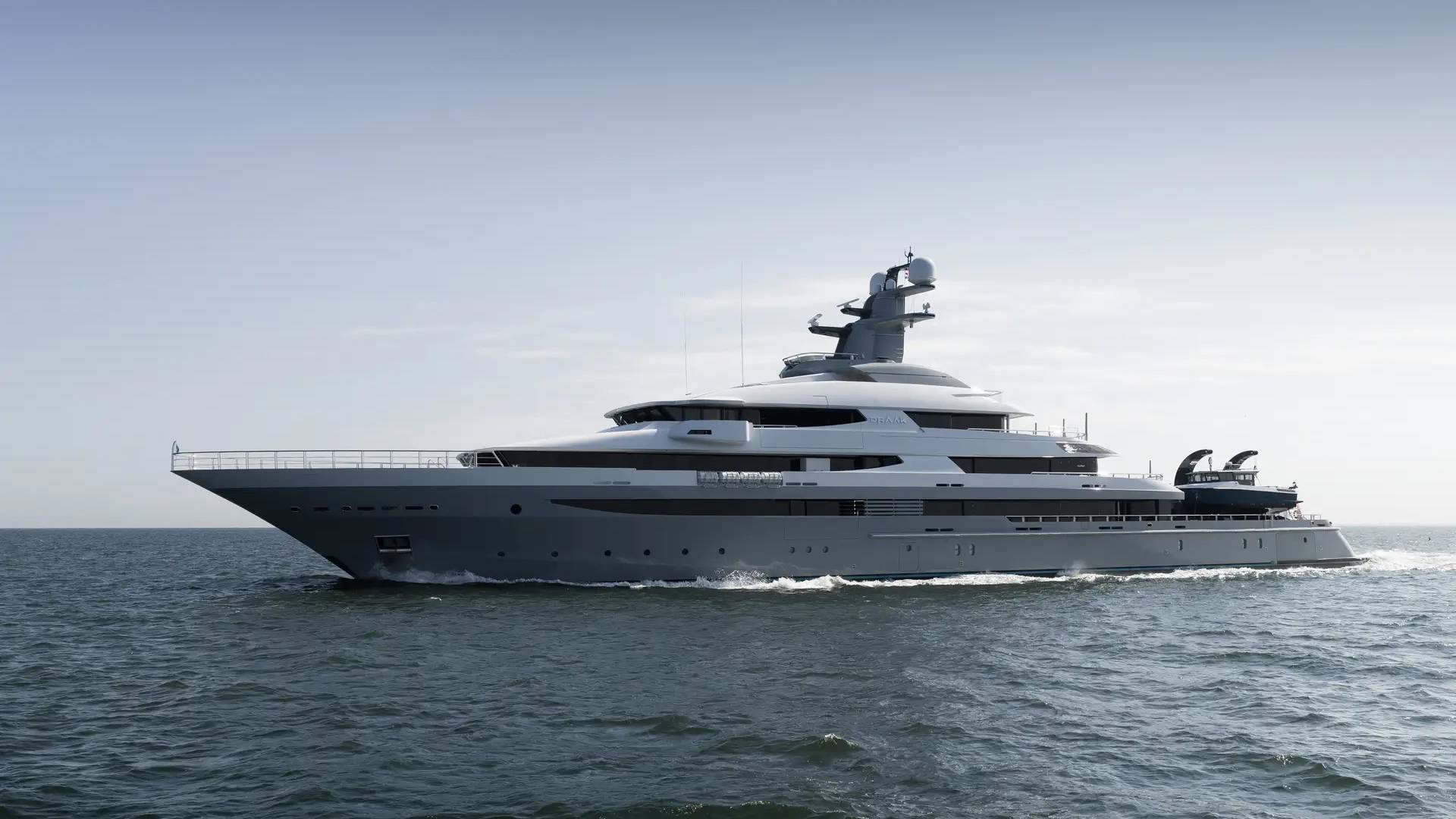 A sleek, gray superyacht cruises on calm, dark blue water under a pale, hazy sky.