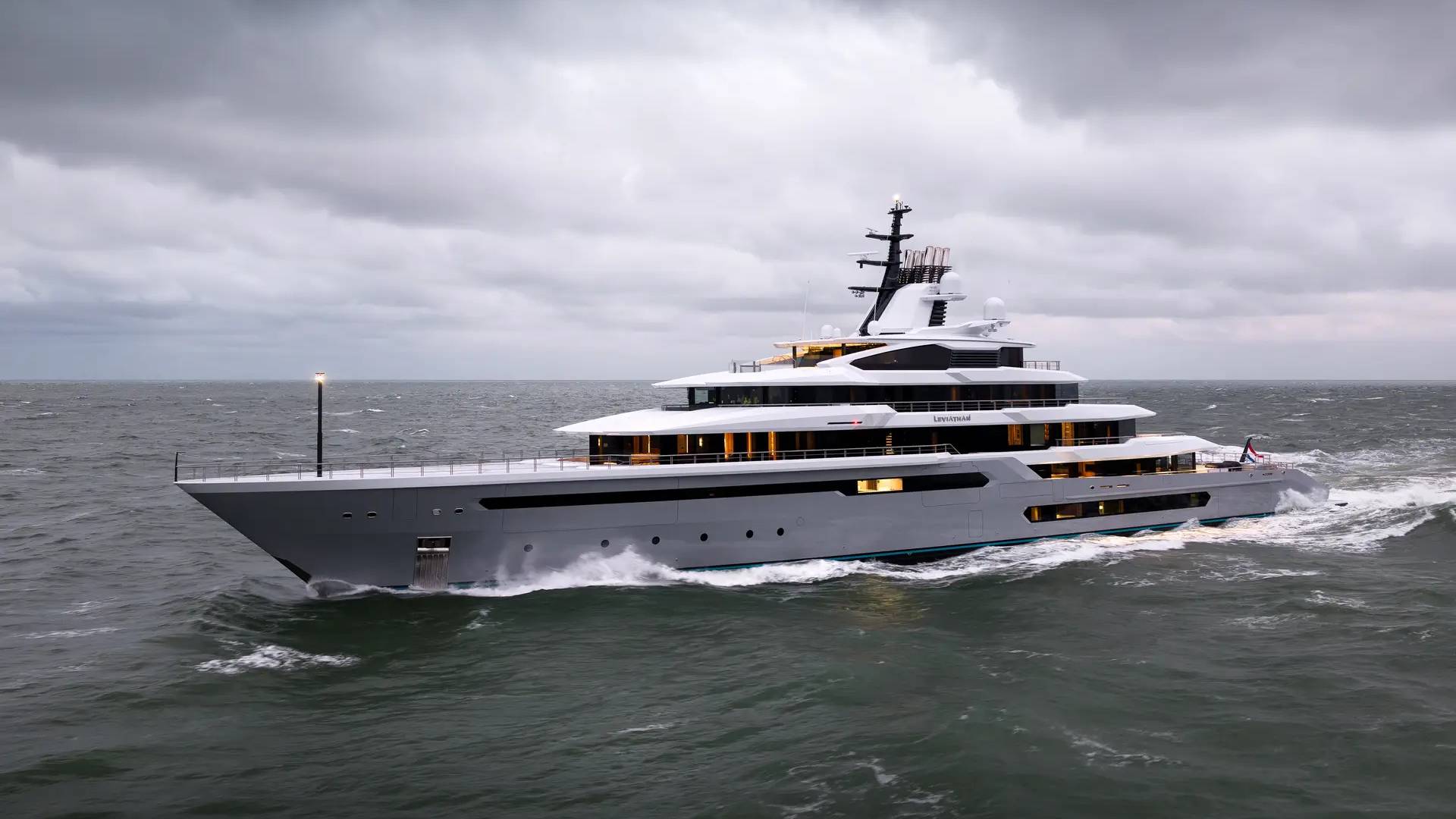 A large, modern gray yacht cruises through choppy, dark water under a cloudy sky.