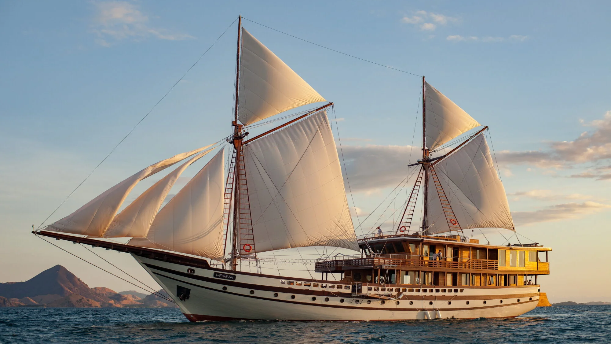 A majestic schooner glides across the shimmering sea under a vast, cloud-dappled sky.