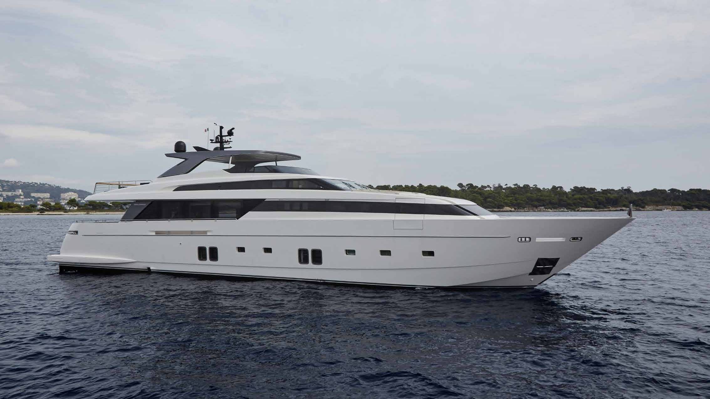 A large, sleek white yacht floating on the calm, dark blue waters, with a mountainous landscape visible in the background.