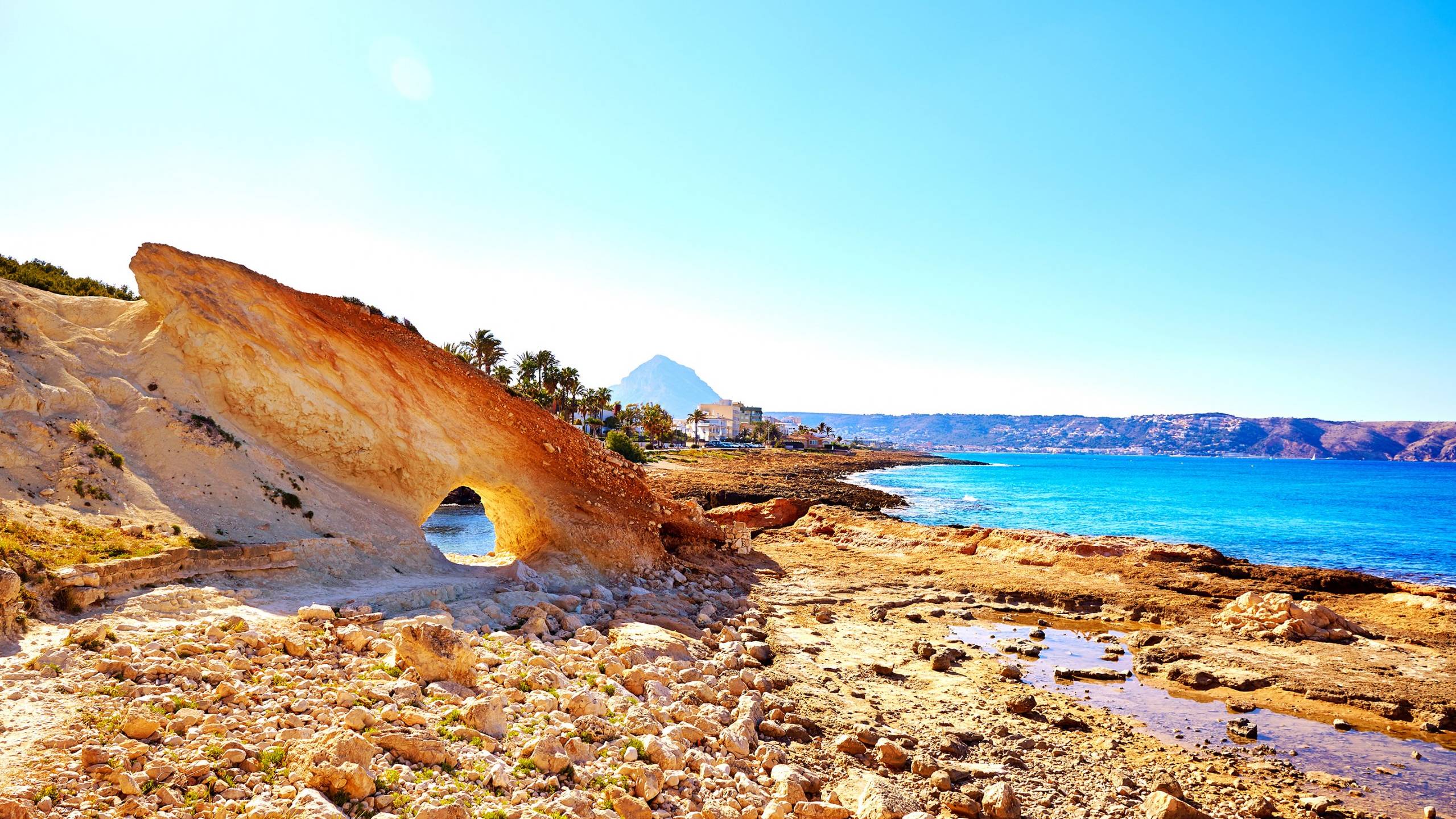 A dramatic rock arch frames the turquoise waters of the Mediterranean Sea under a clear blue sky.