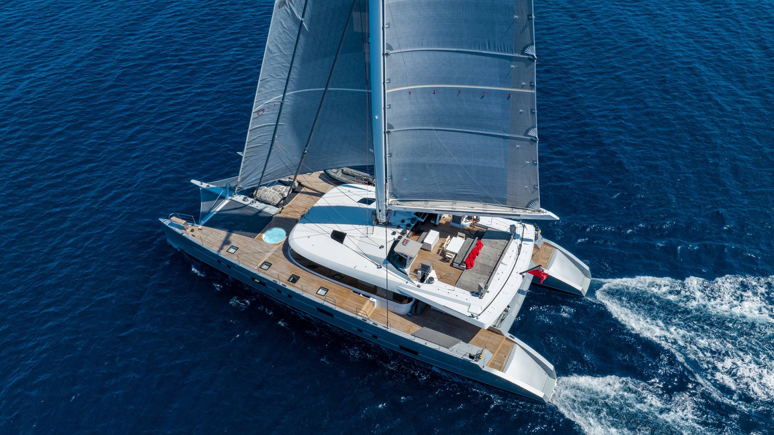 A sleek catamaran glides through the deep blue ocean, its sails catching the wind.