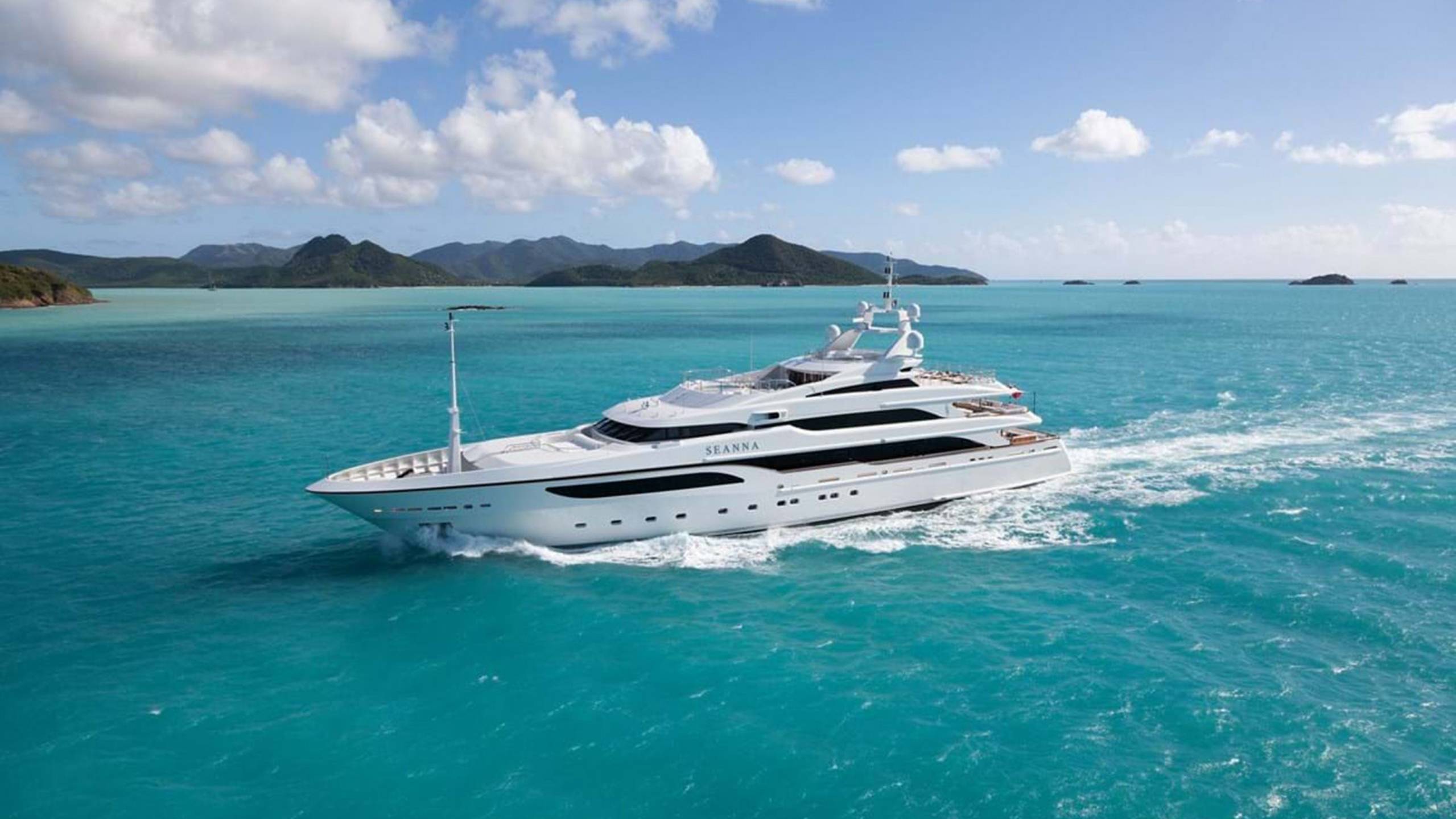 A luxurious white yacht glides through the vibrant turquoise waters of a tropical paradise.