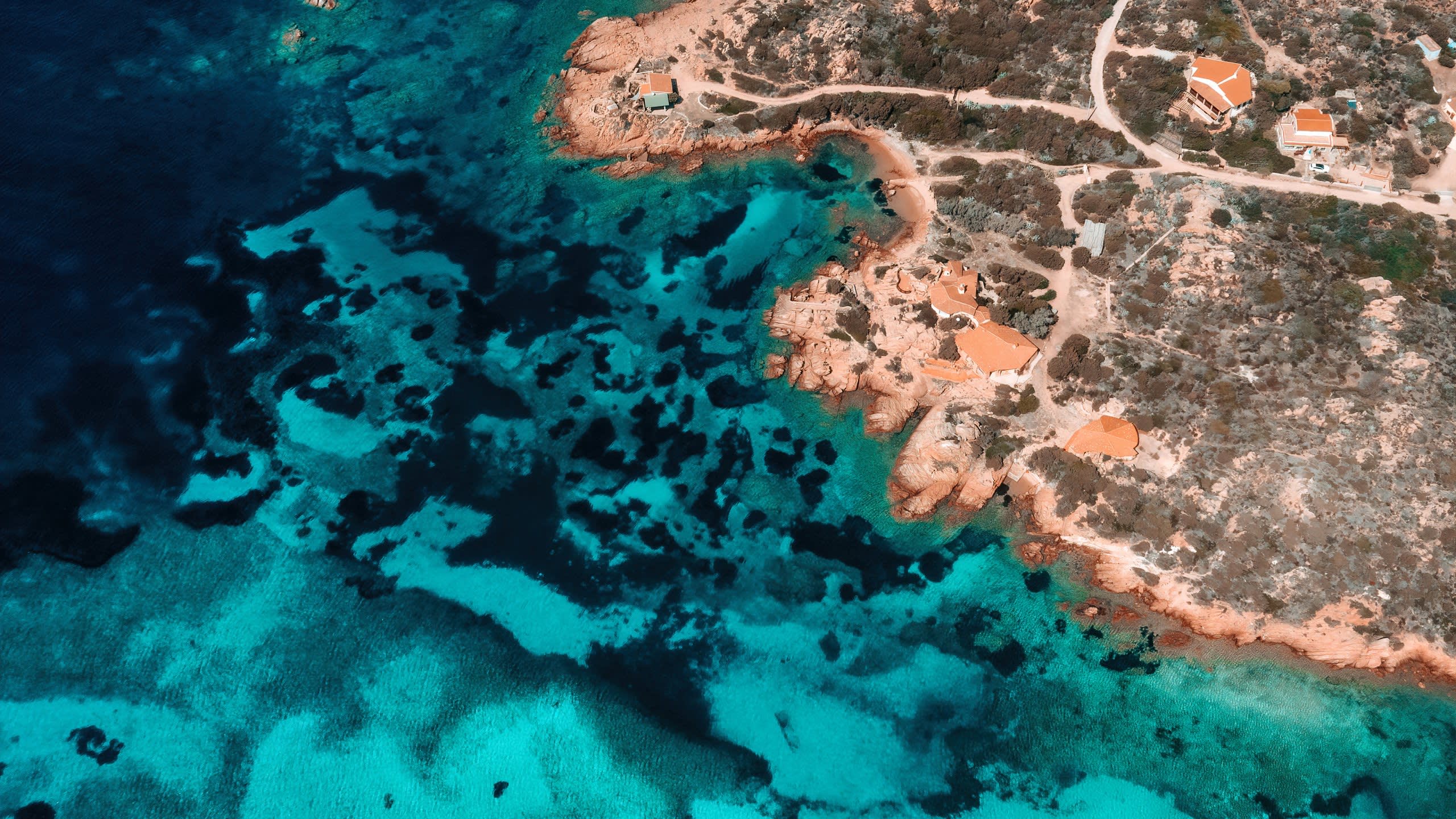Turquoise waters lap against the rocky coastline dotted with charming villas under the Mediterranean sun.