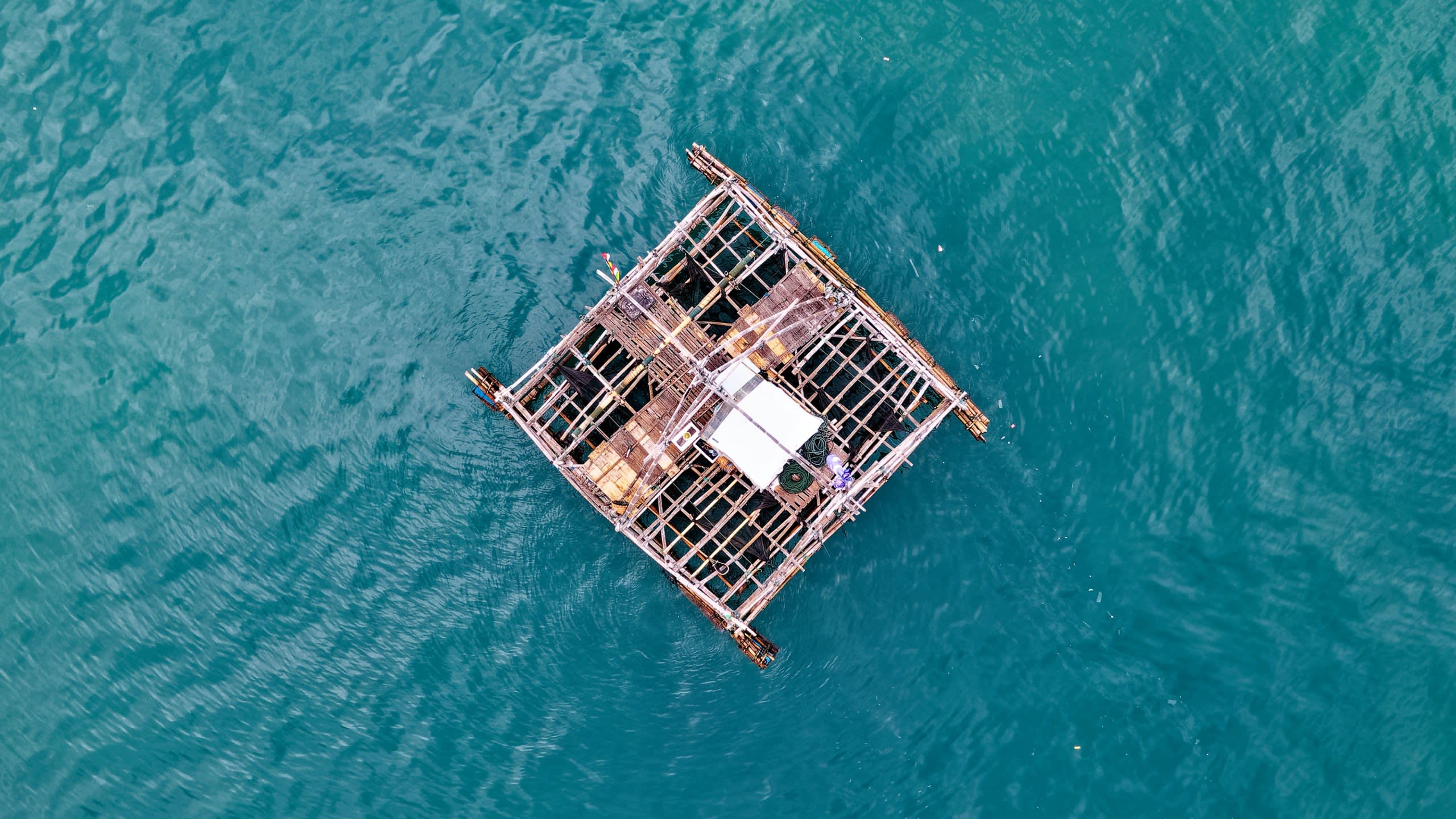A lone figure tends to a rustic bamboo raft floating on the tranquil turquoise waters.