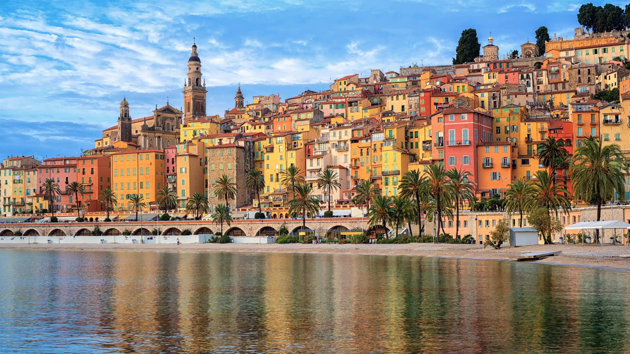 Colorful buildings cascade down a hillside to the tranquil waters of Menton, France.