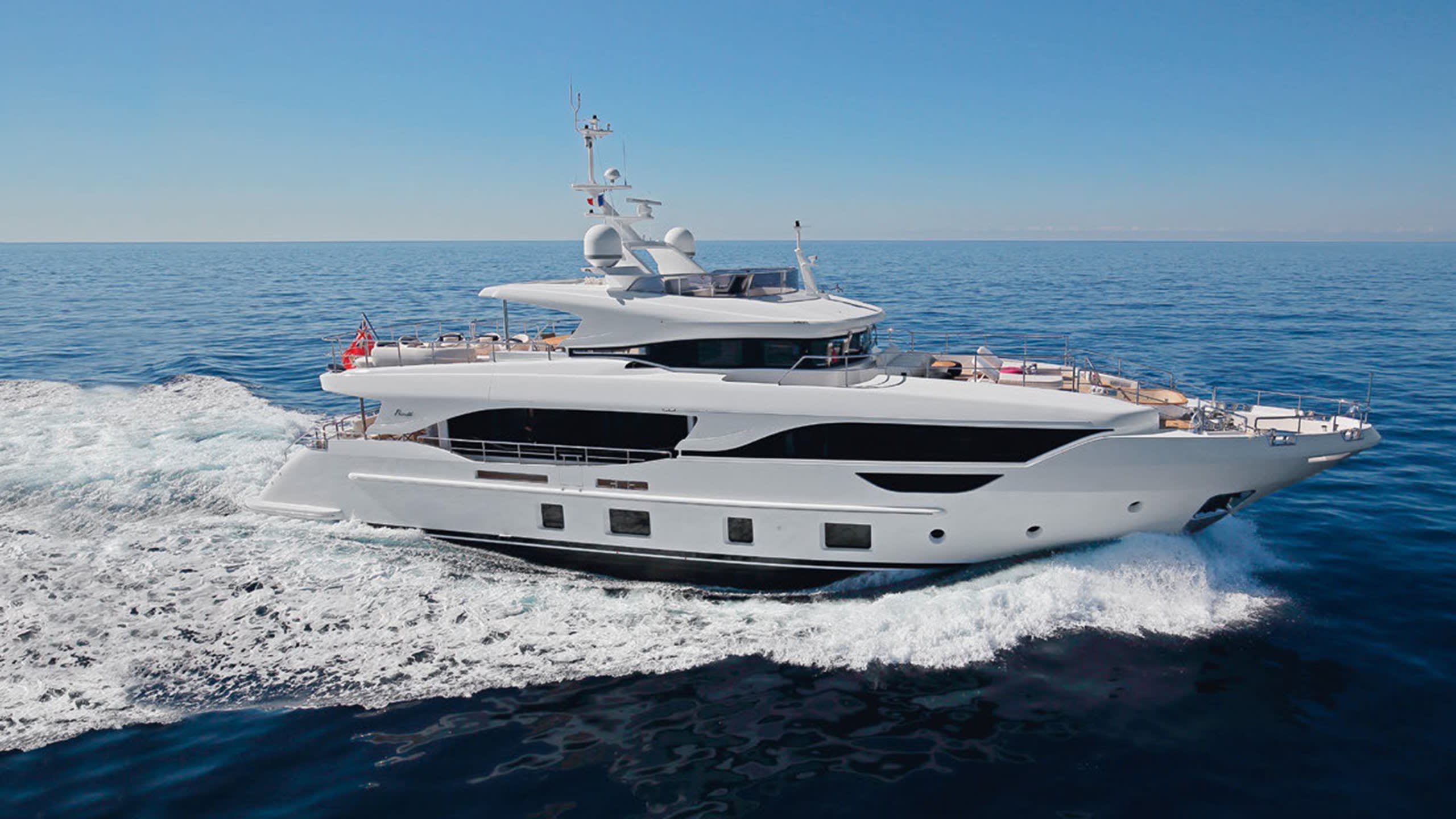 A sleek white yacht glides through the deep blue ocean under a clear sky.
