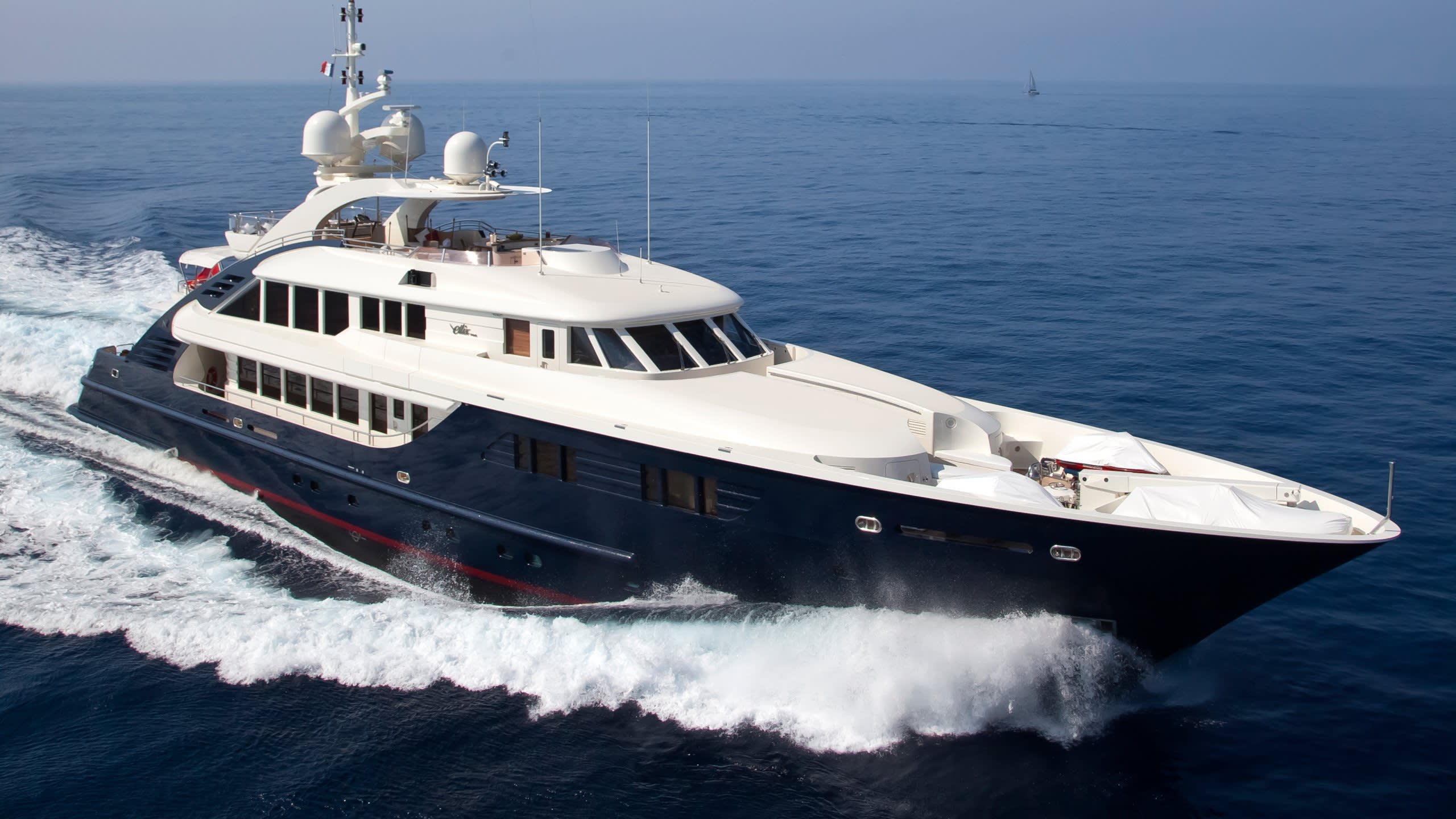 A sleek, dark blue yacht cuts through the azure waters, leaving a foamy wake in its path.