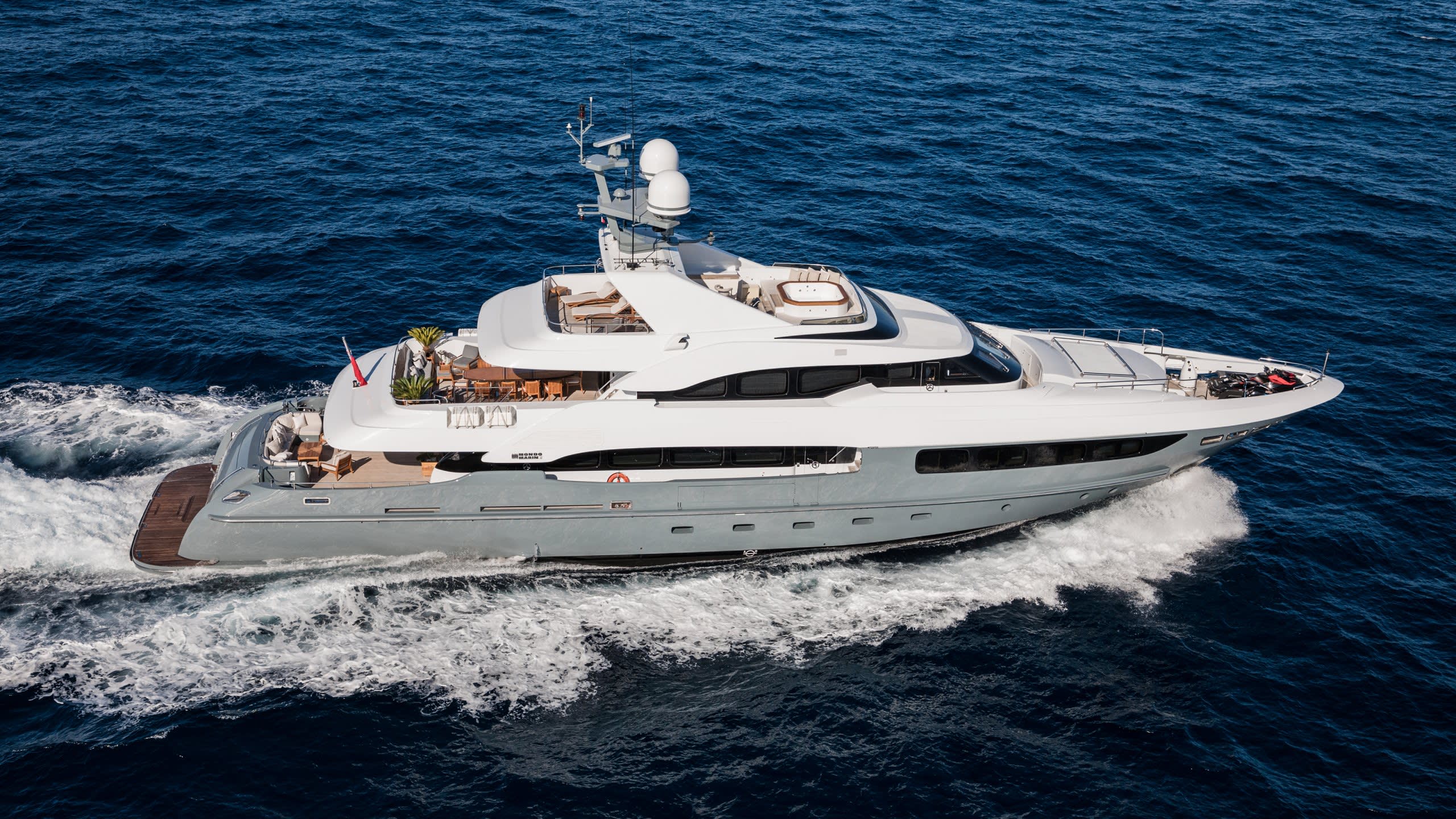 A sleek, modern yacht glides through the deep blue ocean, leaving a trail of white foam in its wake.