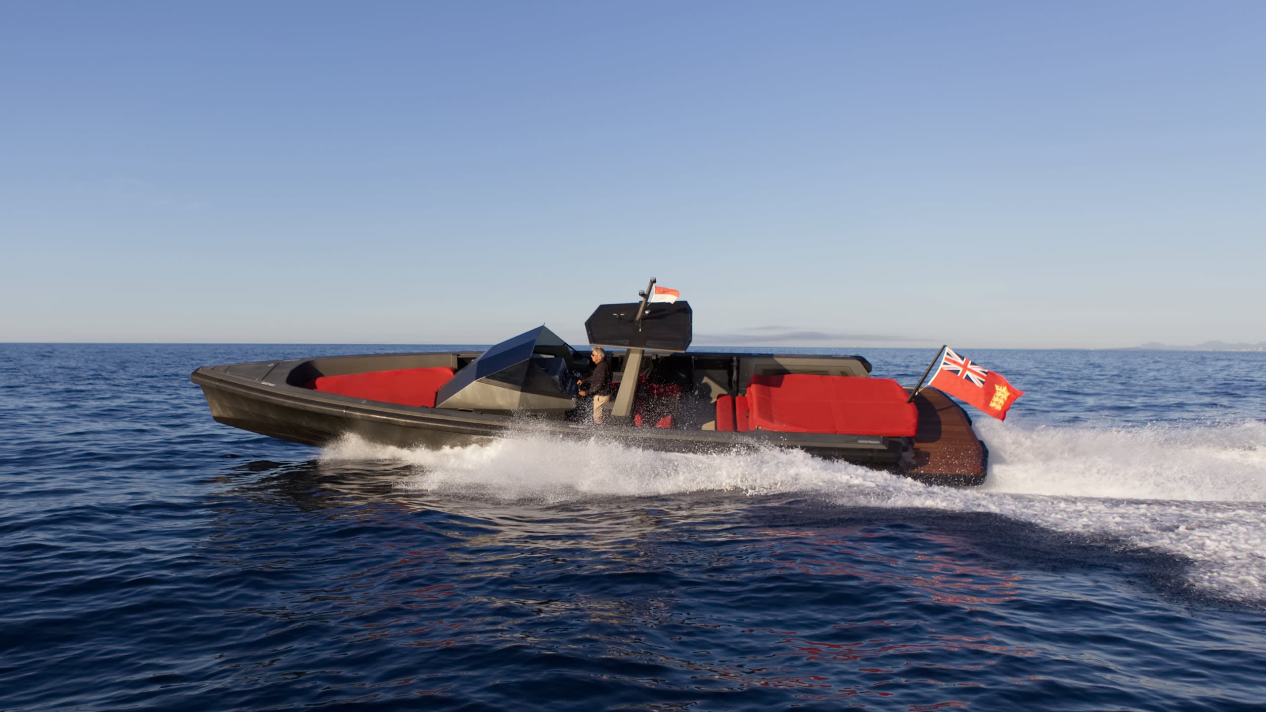 A sleek, dark boat with bright red seating cuts through the deep blue ocean, leaving a trail of white spray.