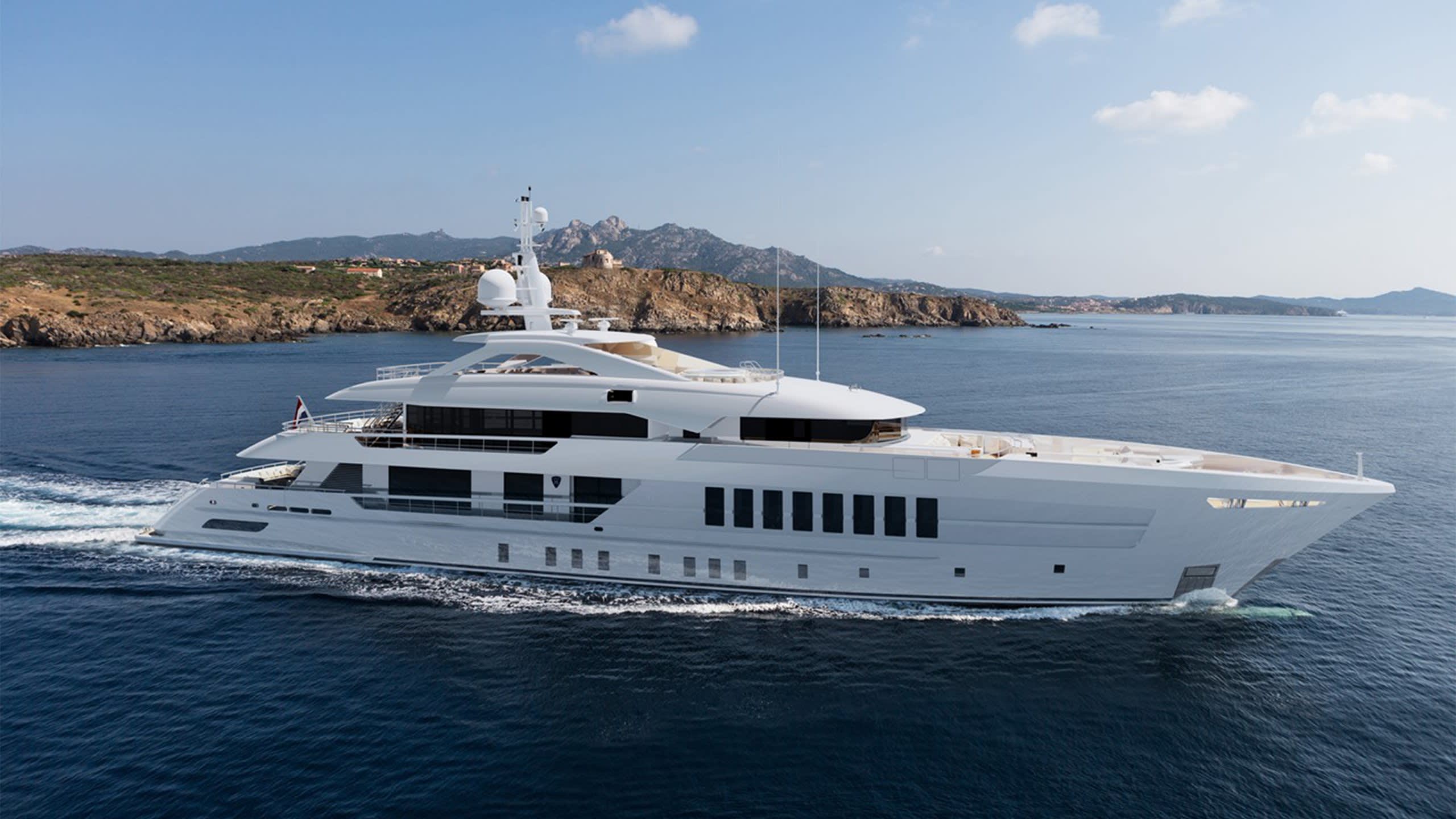 A luxurious white yacht glides through the deep blue sea near a rocky, tree-covered coastline under a clear sky.