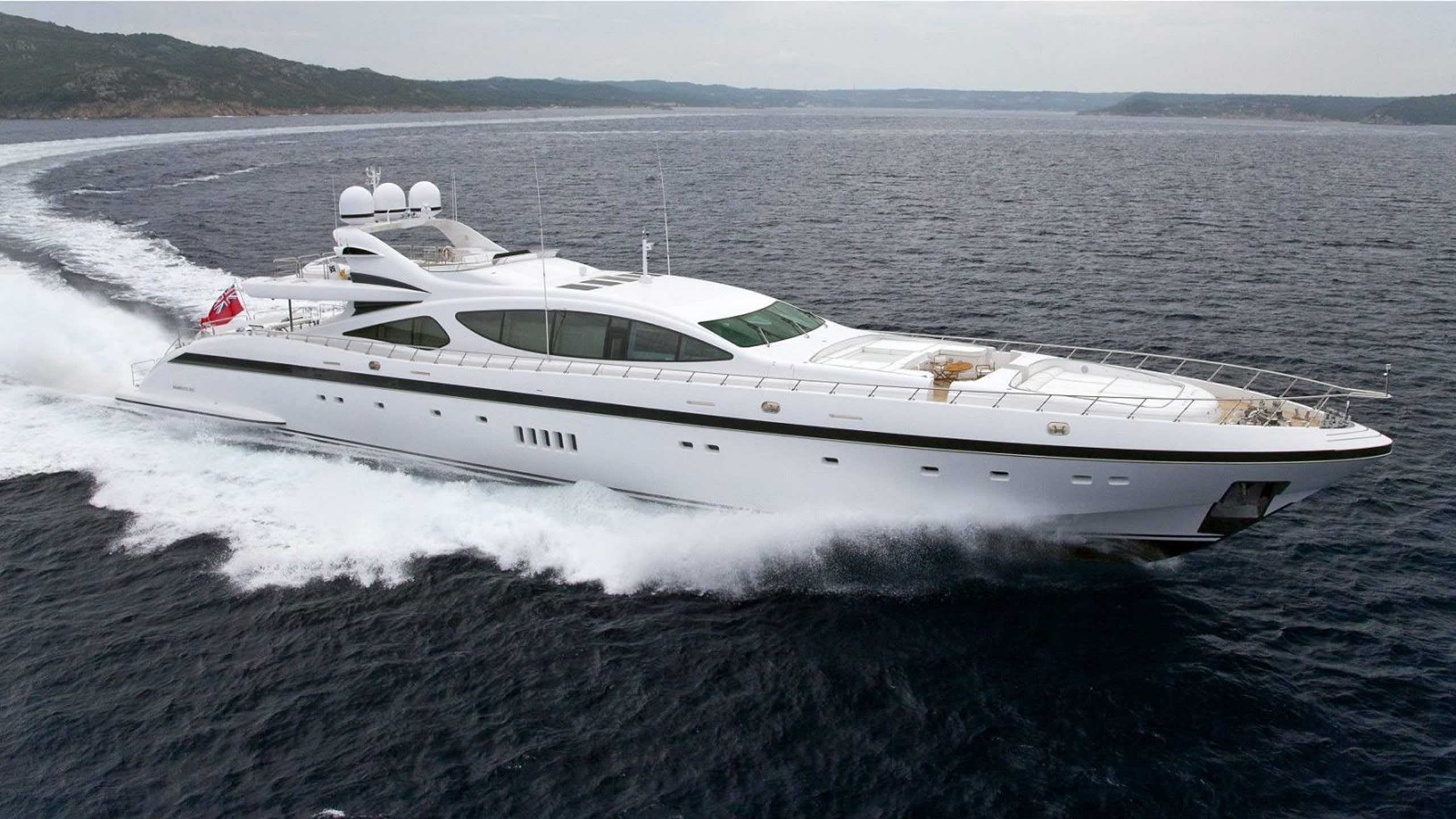 A large, luxurious yacht speeding across the calm, open waters of a scenic coastal landscape with mountains in the background.
