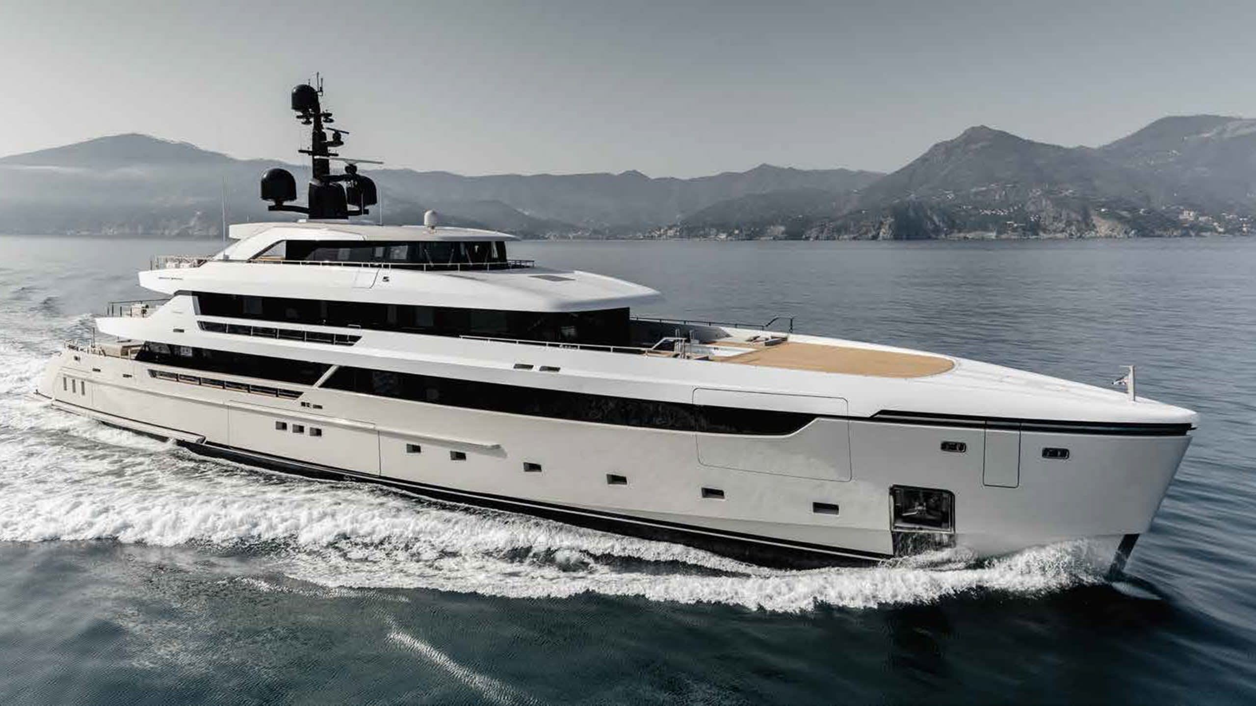 A sleek white yacht glides through the calm blue water, its modern design cutting a sharp silhouette against the misty mountains.