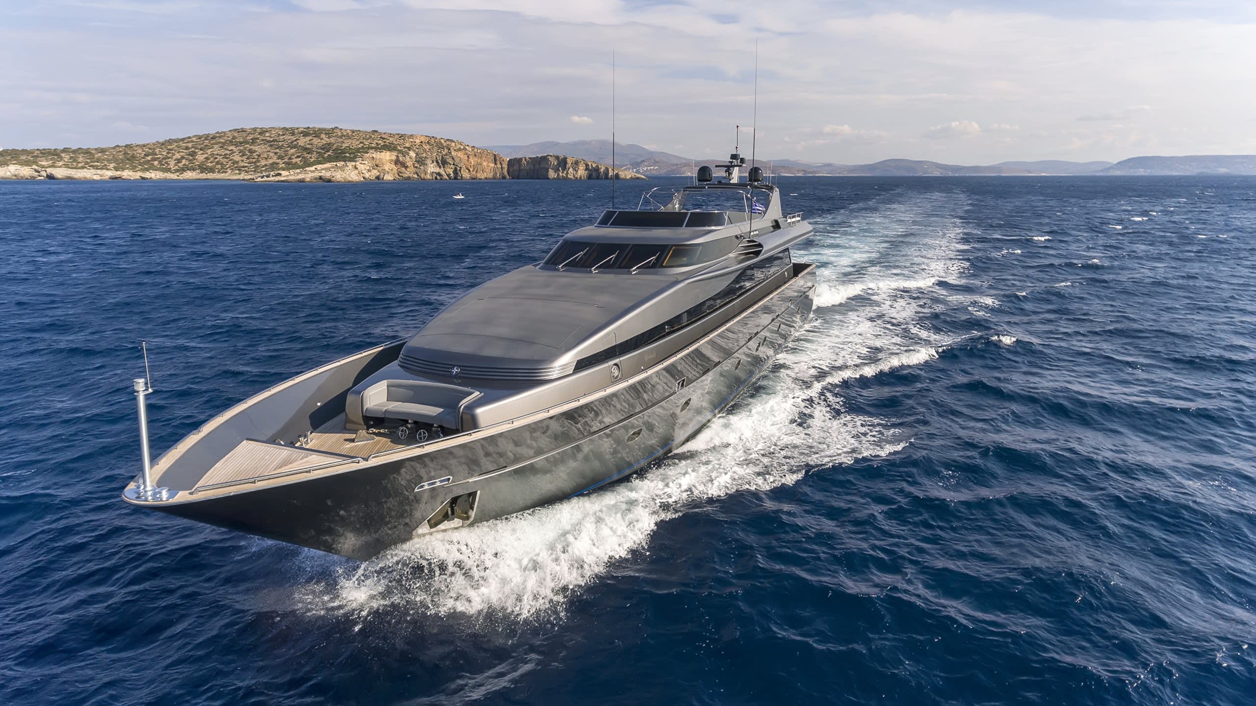 A sleek, modern yacht cruises through the deep blue sea, leaving a foamy wake against a backdrop of rugged islands.