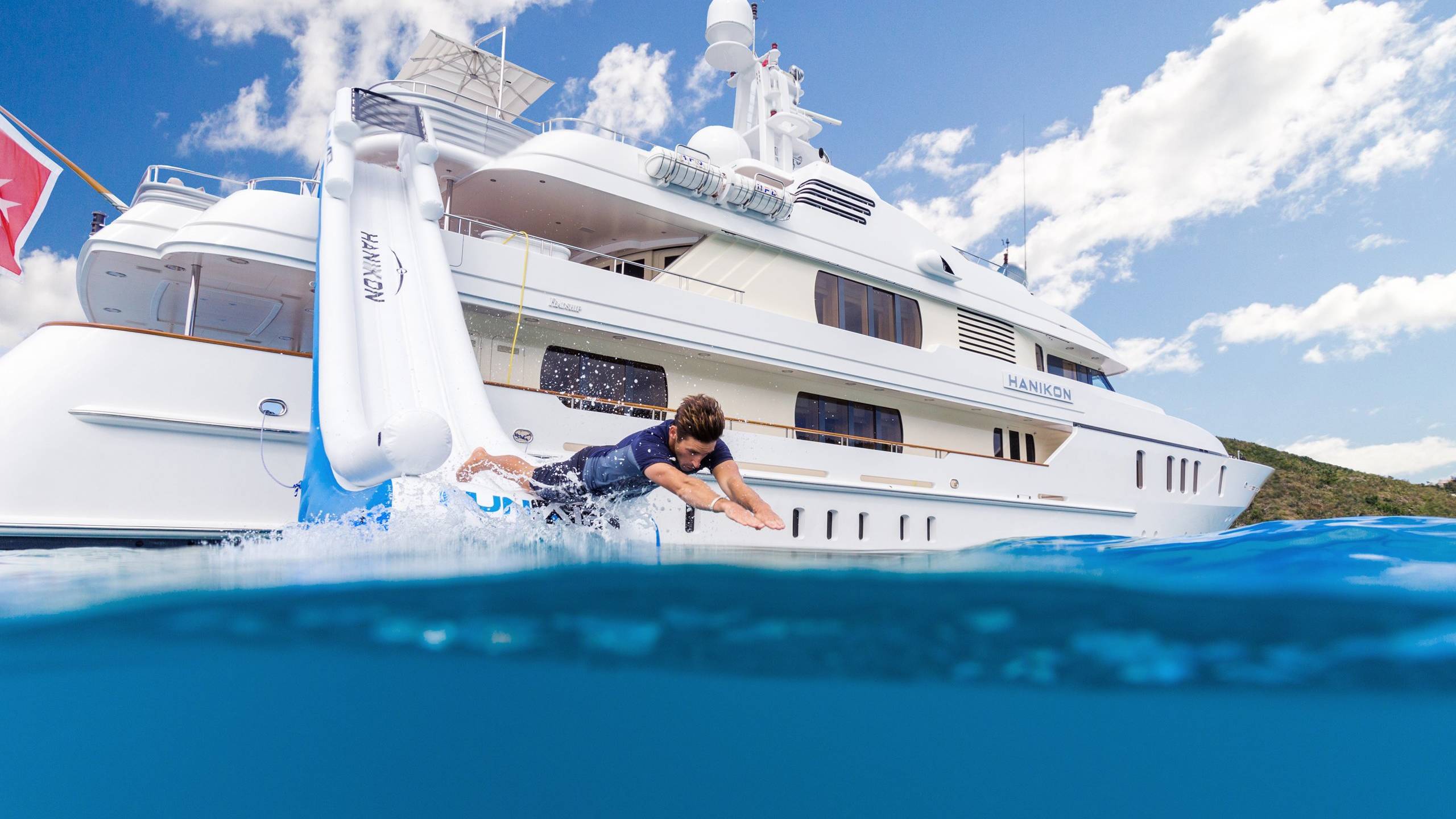 A man dives off a yacht's inflatable slide into the clear blue ocean.