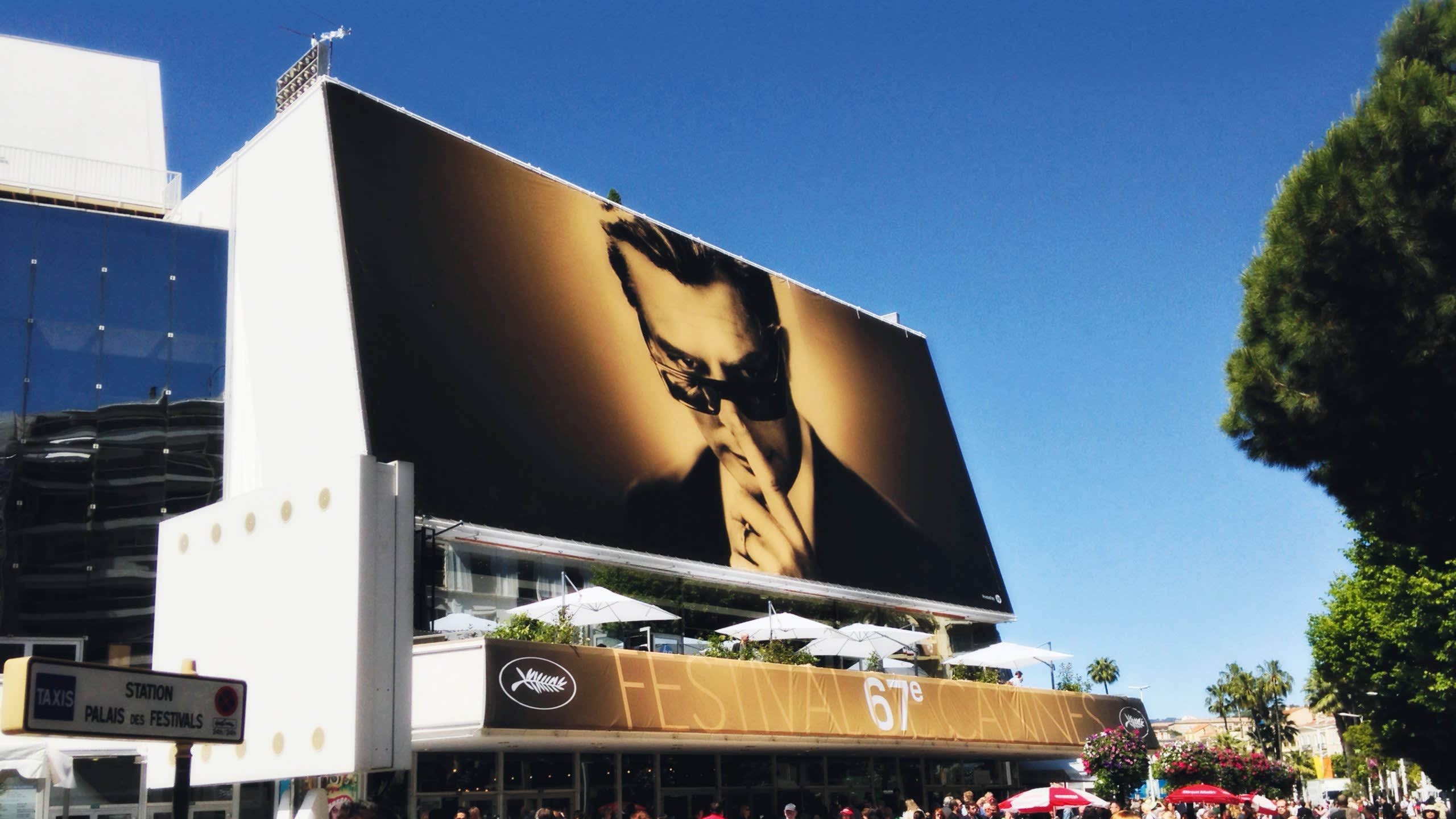A giant billboard of a man in sunglasses overlooks the bustling 67th Cannes Film Festival.