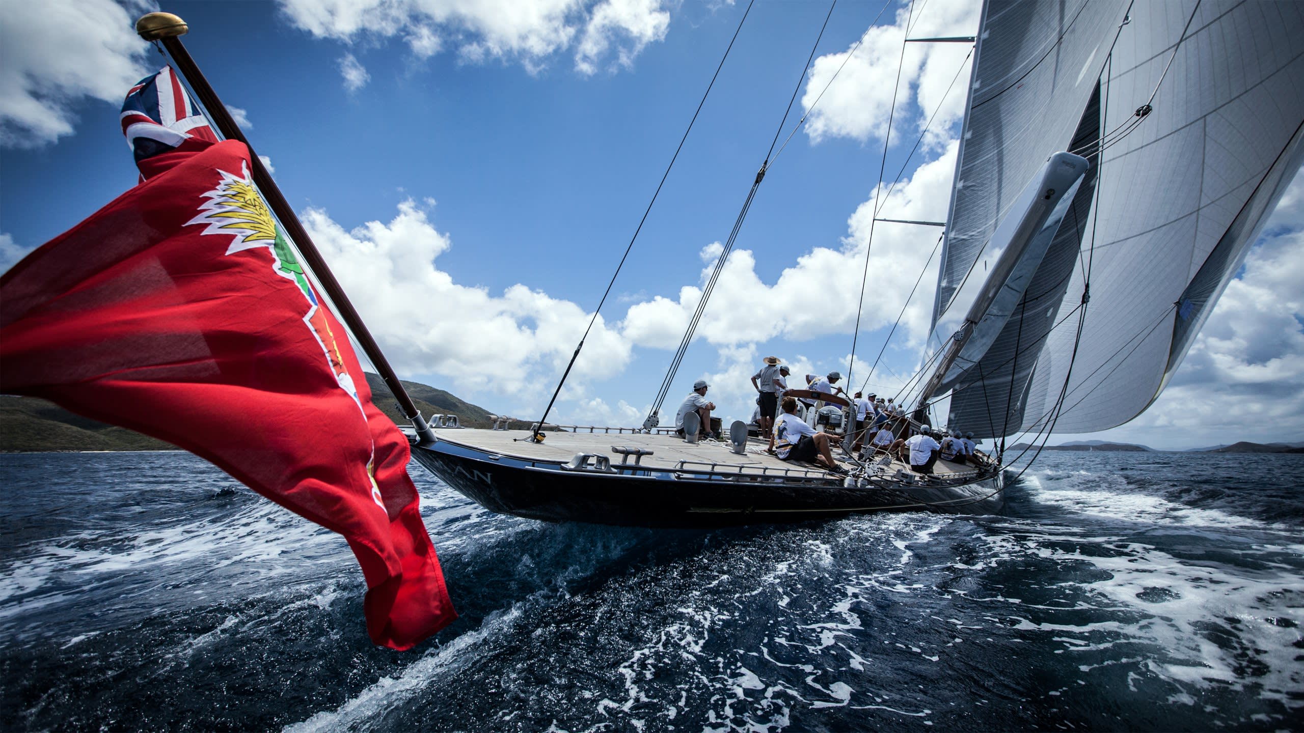 A majestic yacht cuts through the waves under a bright blue sky with fluffy clouds.
