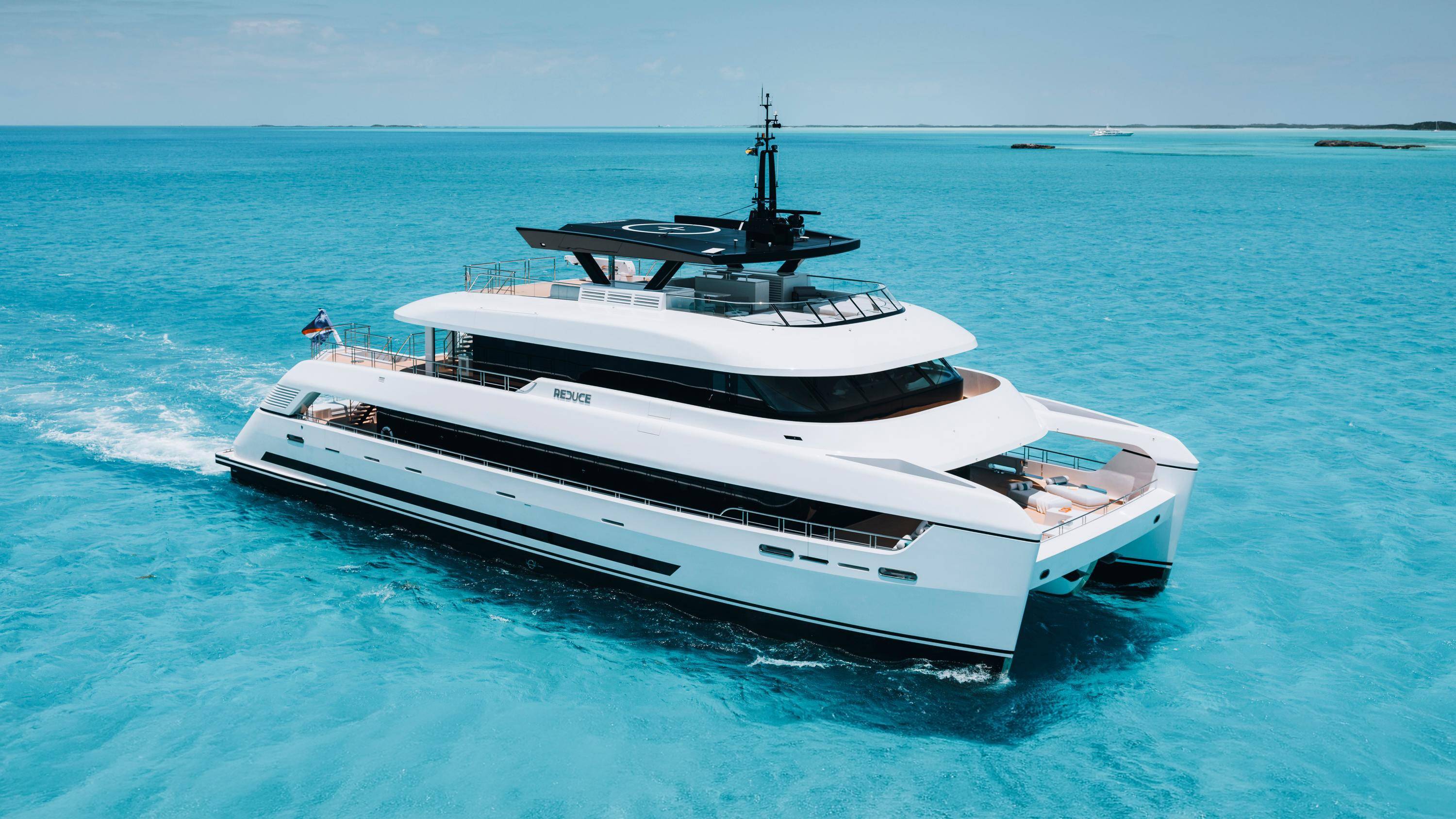 A sleek white catamaran yacht glides through crystal-clear turquoise waters under a bright blue sky.