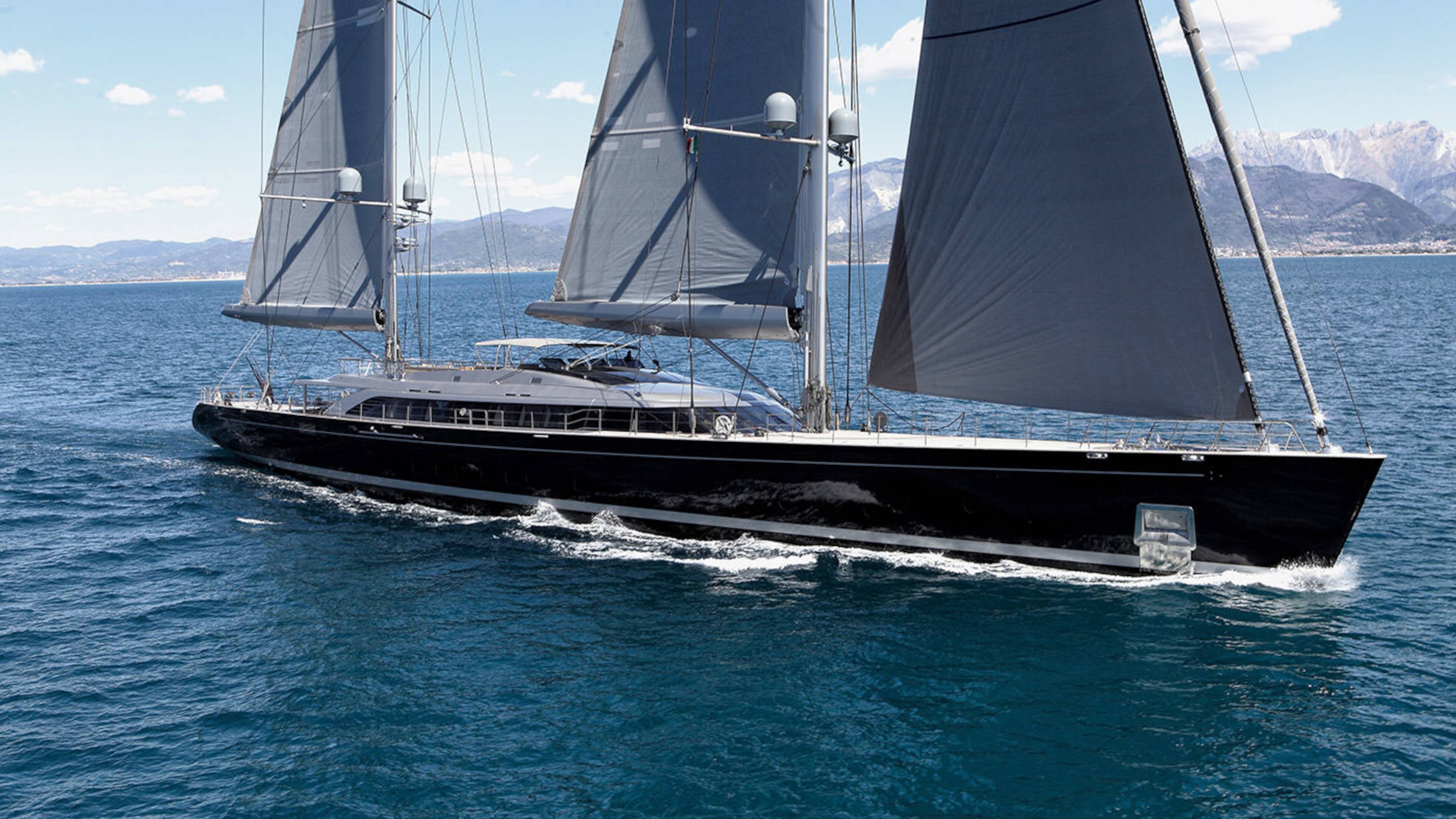 A sleek black yacht with dark sails glides through the deep blue sea under a bright sky.