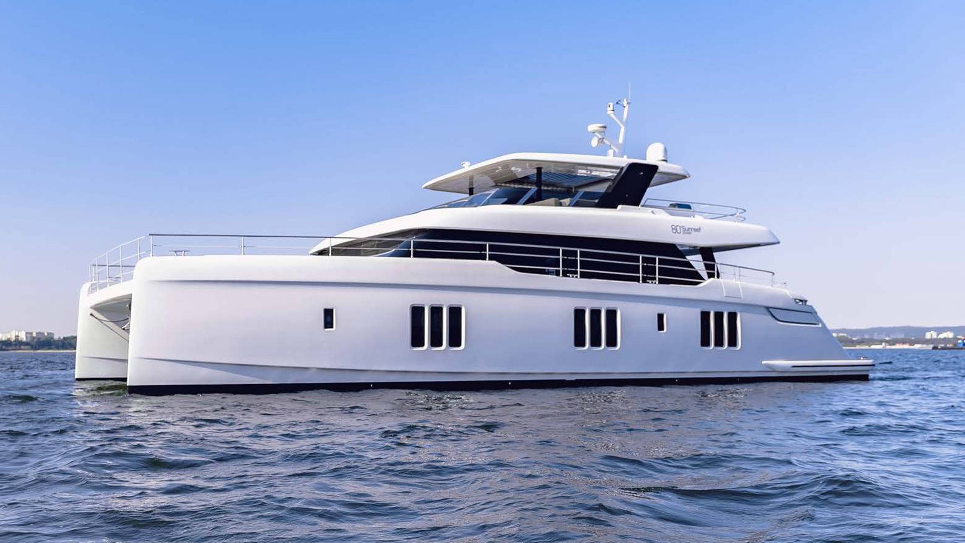 A sleek white catamaran yacht glides across the calm blue water under a clear sky.