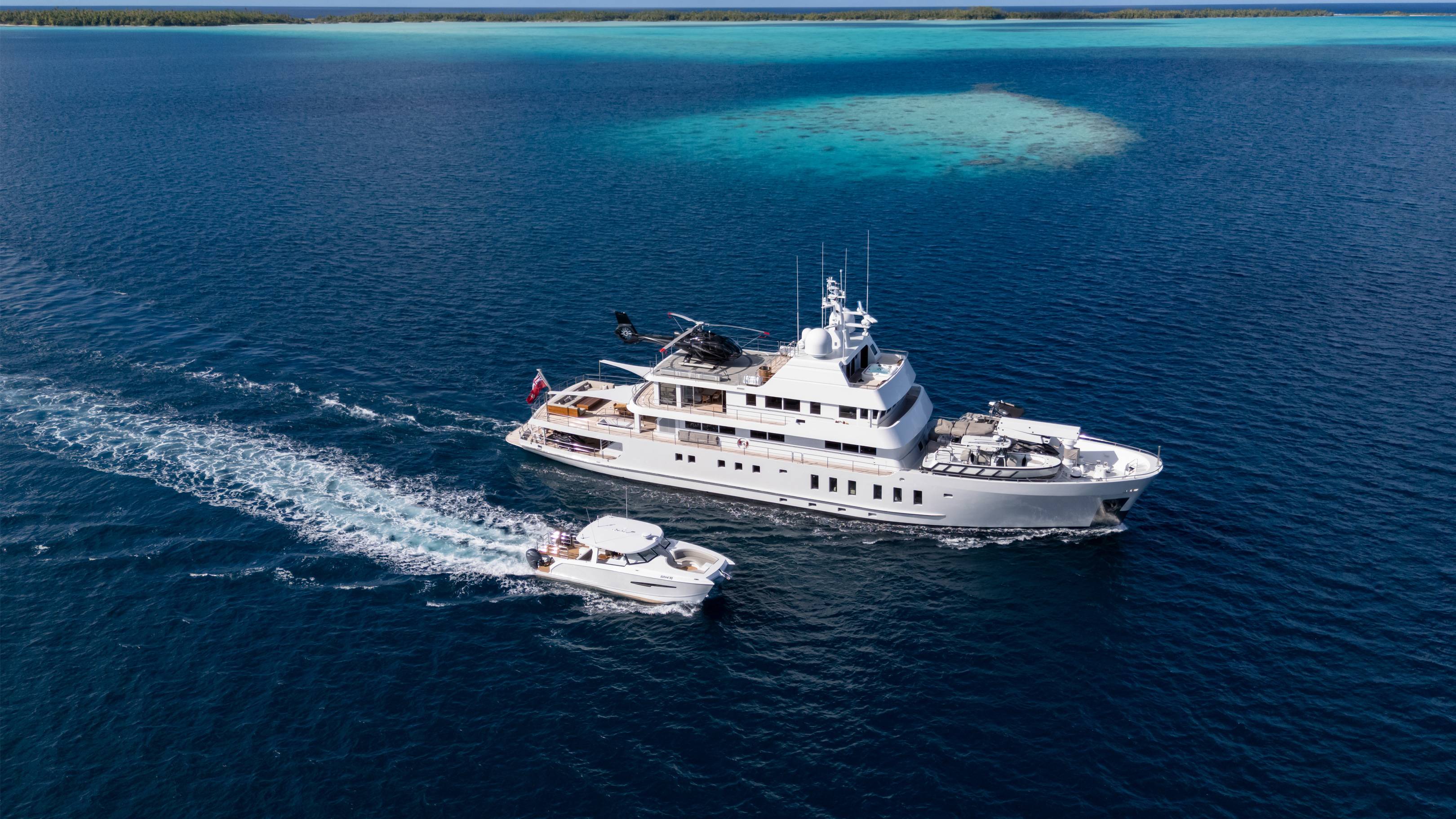 A luxurious superyacht and its tender cruise through the crystal-clear turquoise waters of a tropical atoll.
