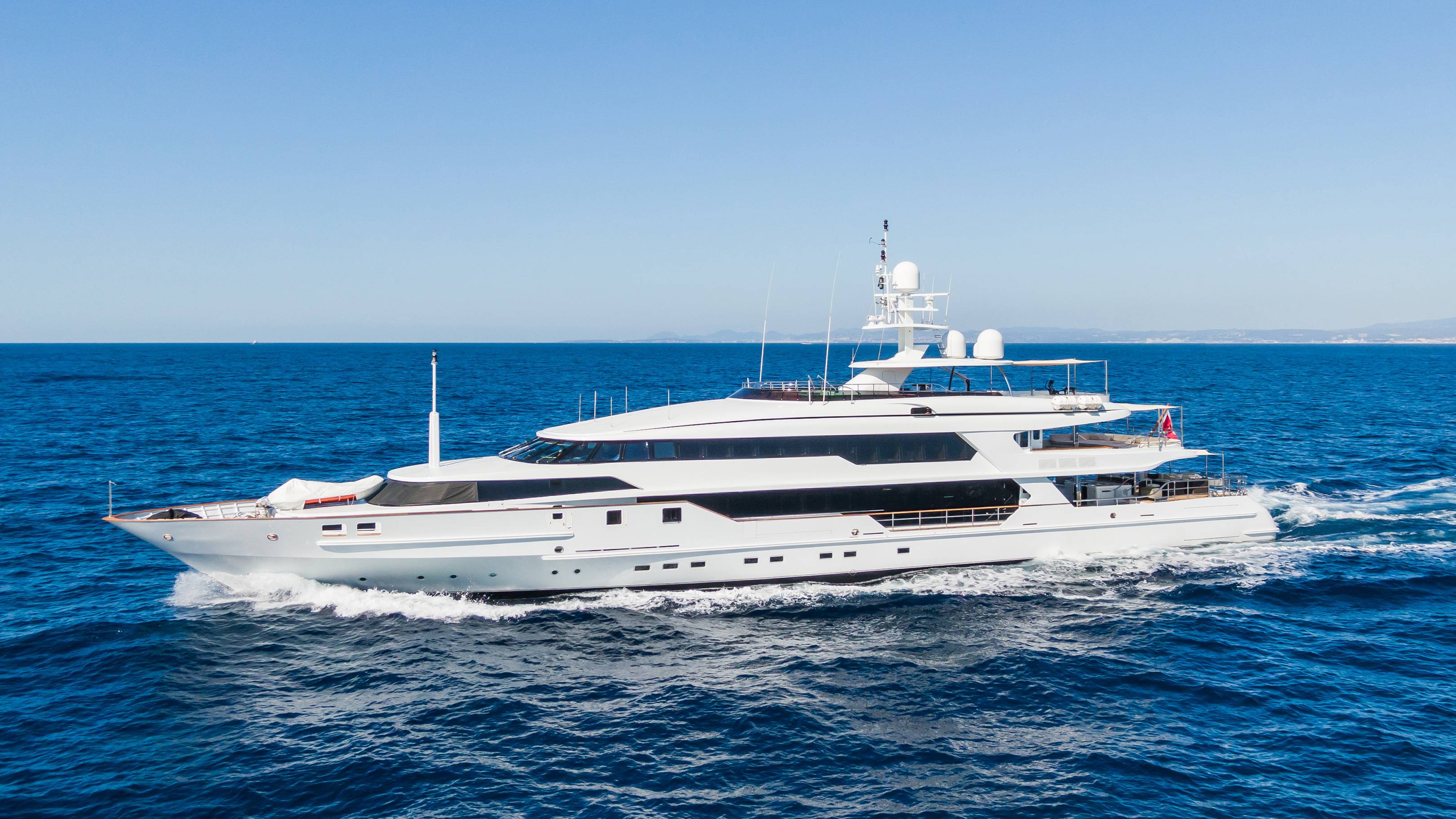 A large white yacht cruises through the deep blue ocean under a clear sky.