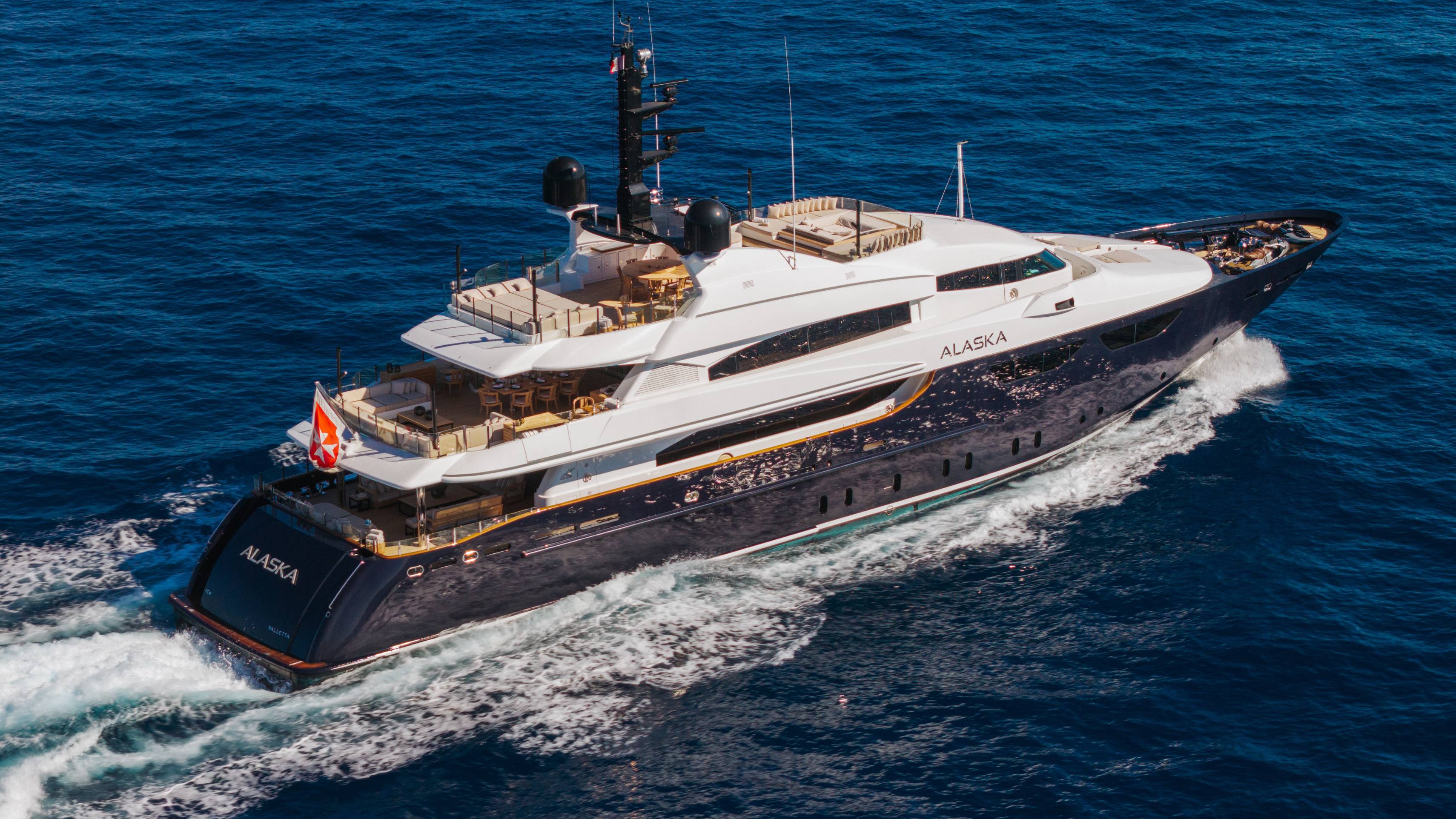 A luxury yacht named "Alaska" cruises through deep blue ocean waters, leaving a white wake in its path.
