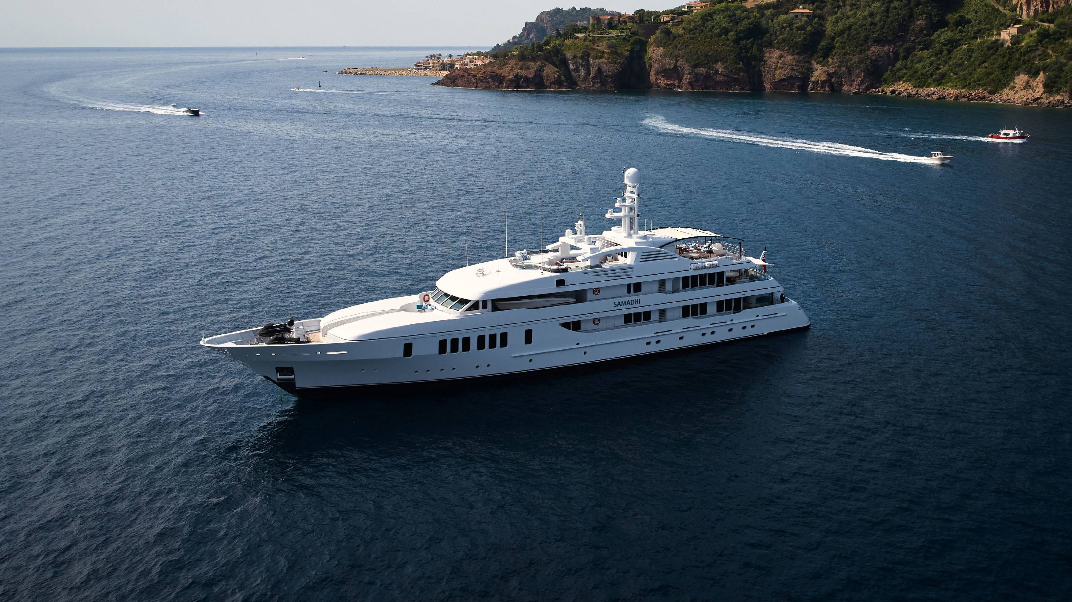 A luxurious white yacht cruises through the deep blue sea near a picturesque coastline dotted with villas.