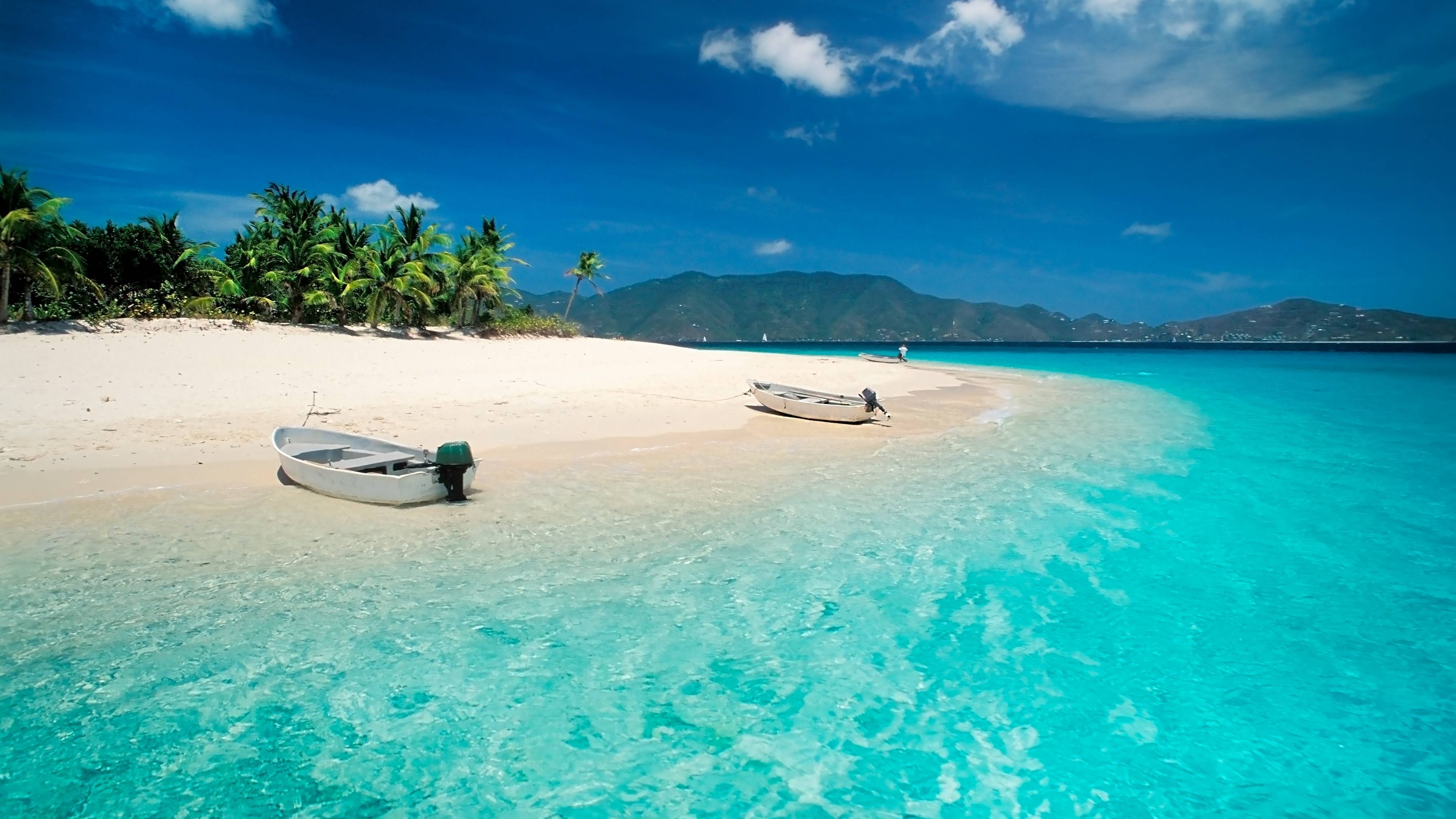 A pristine white sand beach meets crystal-clear turquoise waters with two small boats resting on the shore.