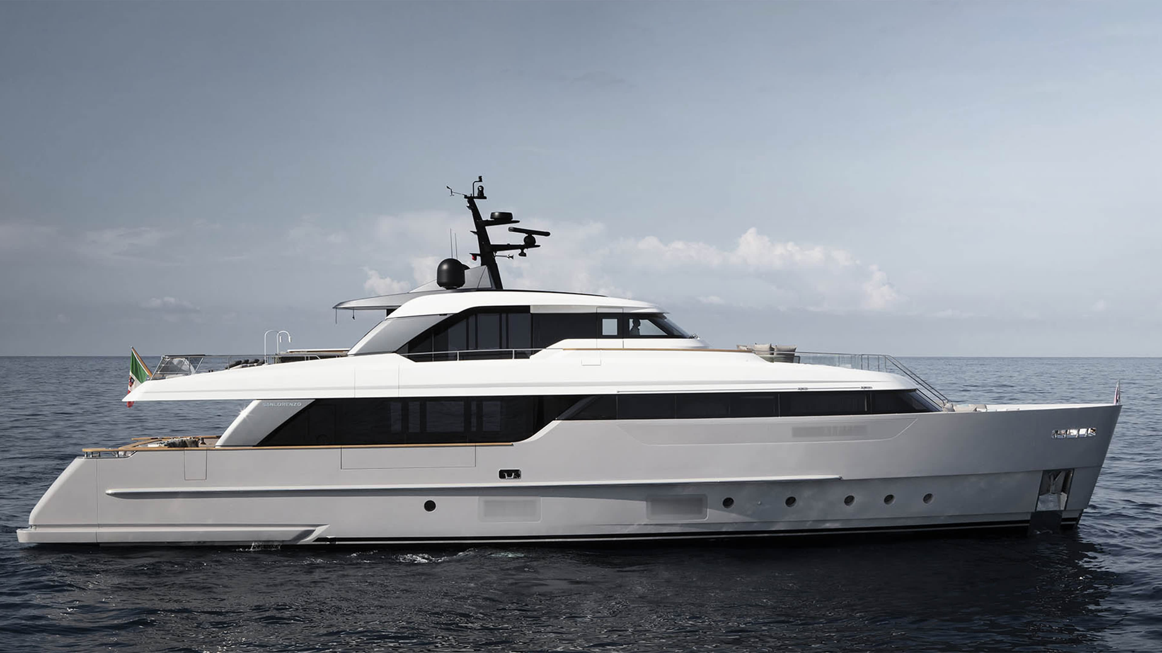 A large, sleek white yacht floating on the calm, blue ocean with a clear sky in the background.