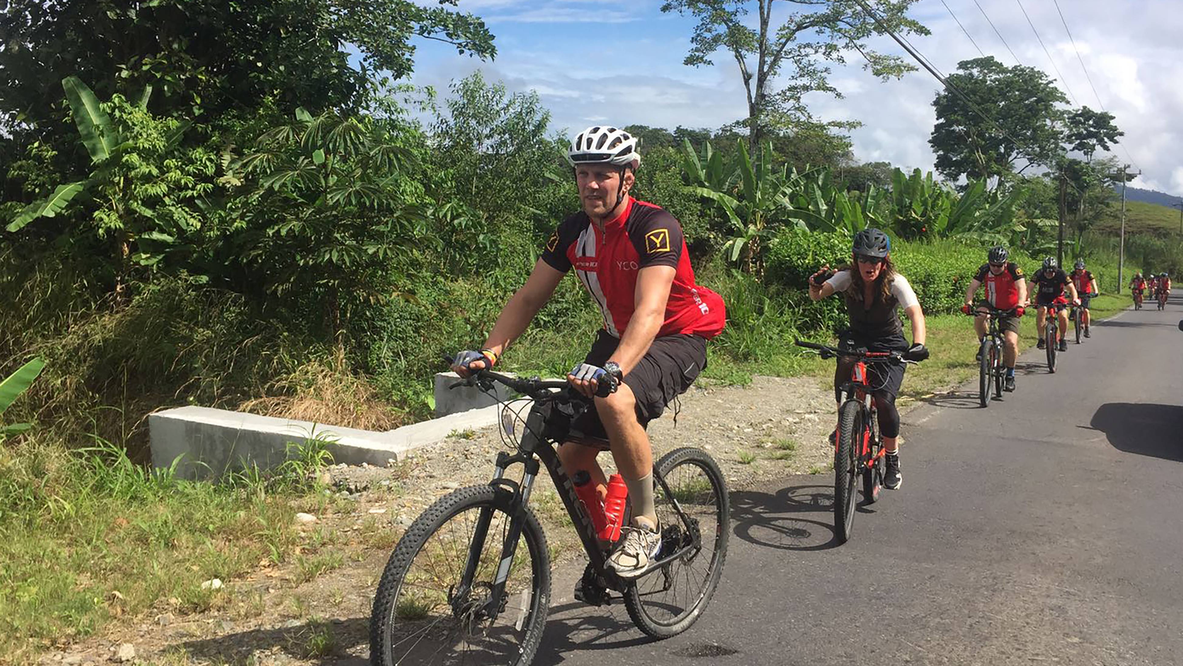 A group of cyclists enjoys a scenic ride through lush green countryside under a partly cloudy sky.