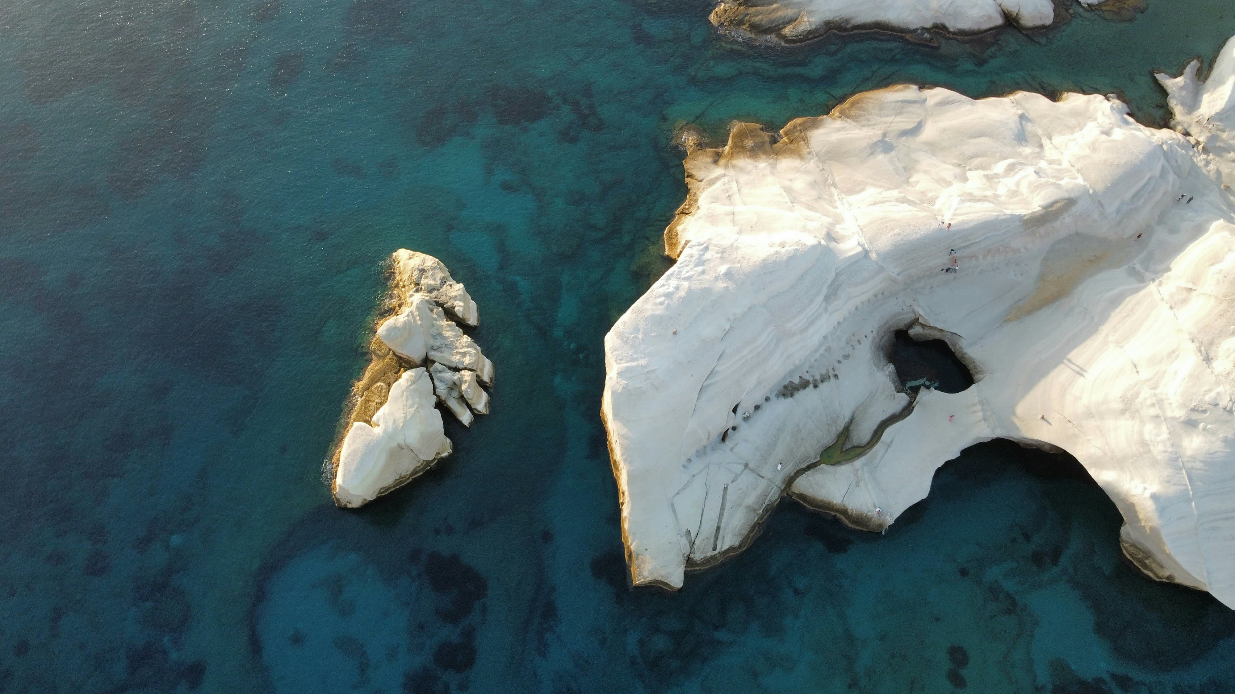 White rock formations rise from the clear turquoise water, with a smaller rocky island in the foreground and a larger, sculpted cliff face in the background.